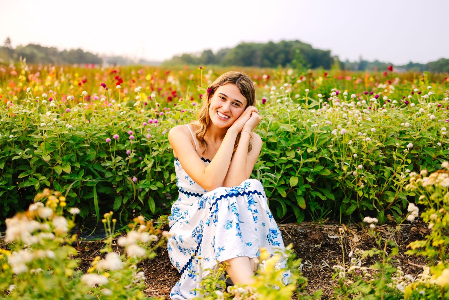A high school senior in a wildflower meadow with blooming poppies and daisies in golden sunlight at Ward's Berry Farm in Sharon MA