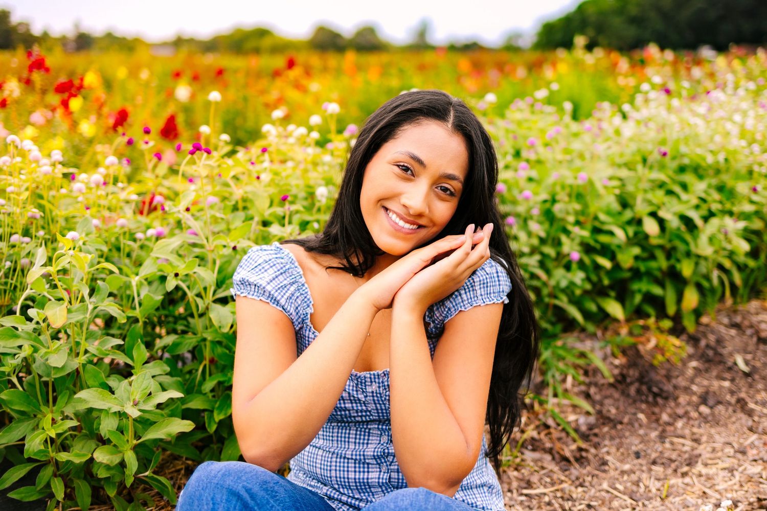 A high school senior in poses joyfully in a field of wildflowers for senior portraits at Wards Berry Farm in Sharon, Massachusetts