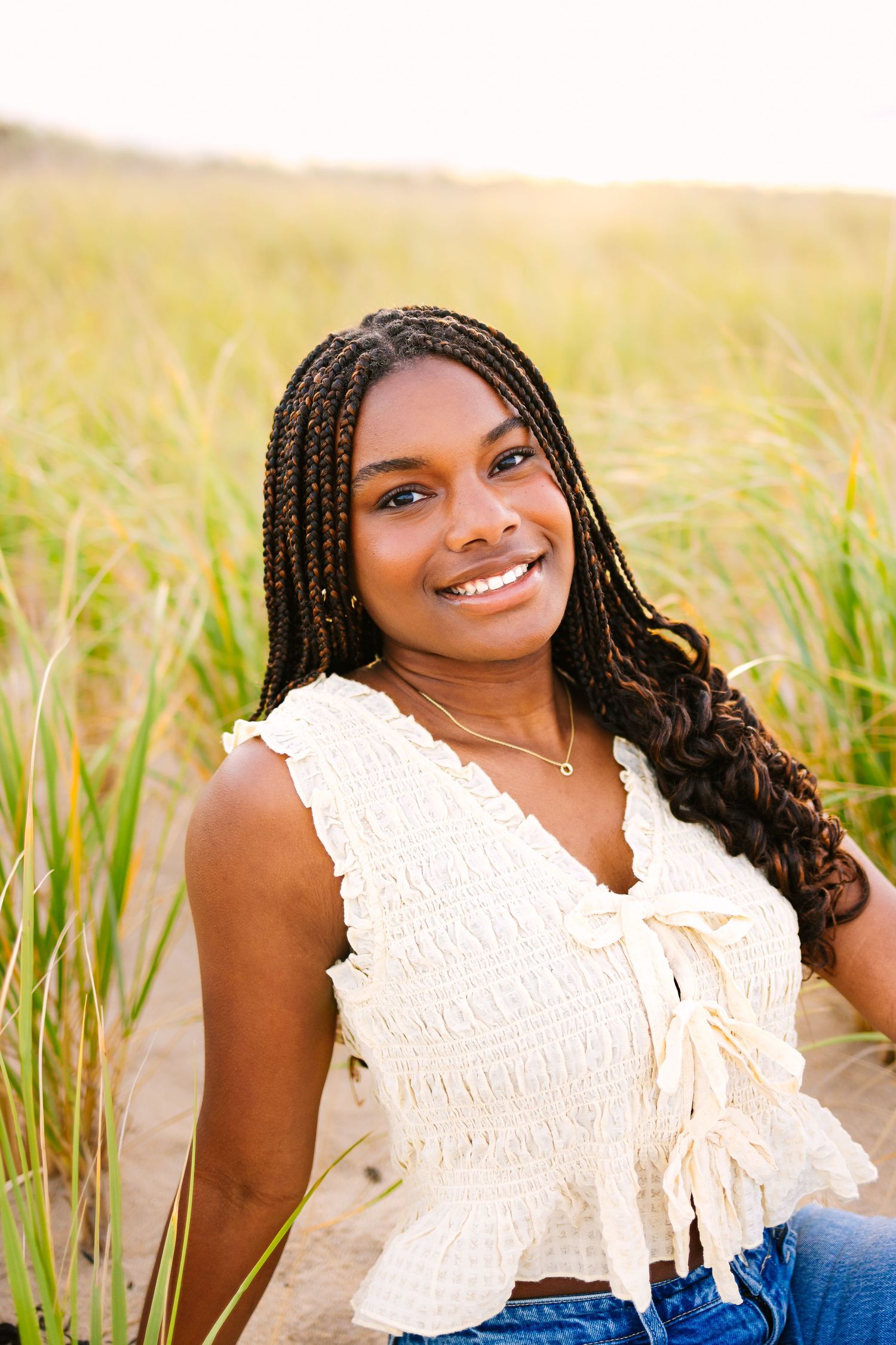 A high school senior sitting by the seagrass at sunset golden hour for senior photos at Scusset Beach in Cape Cod Massachusetts