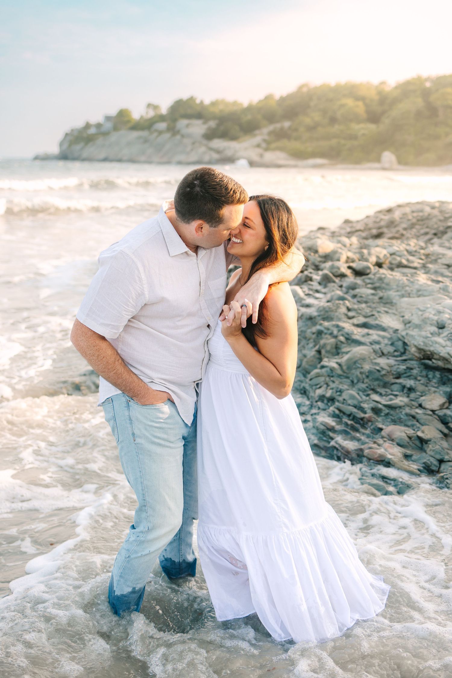 A romantic couple shares a tender moment on a rocky beach shoreline during sunset golden hour engagement photos at Second Beach in Newport