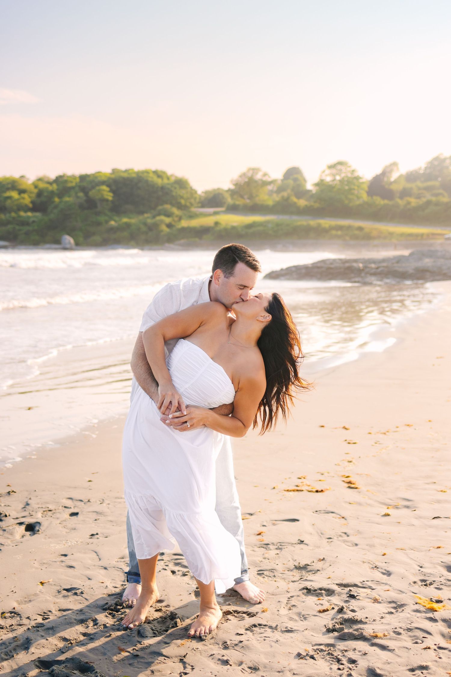 A romantic beach scene at sunset golden hour with a couple in white embracing on the sandy shore at Second Beach in Newport Rhode Island