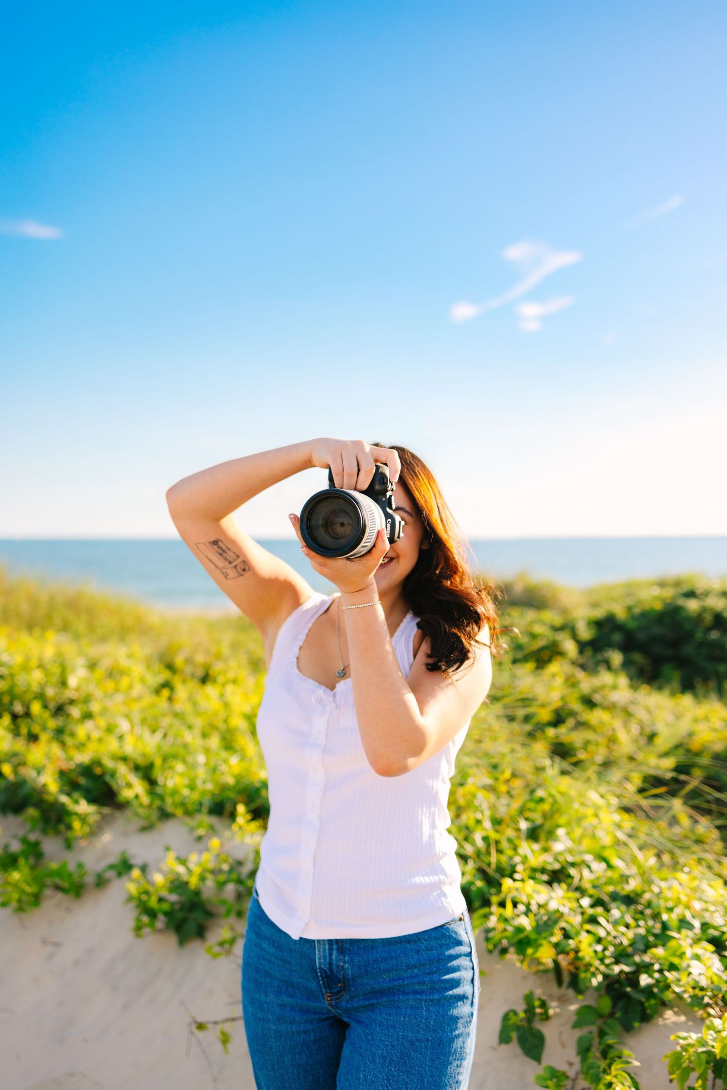 Photographer looking through her camera for branding photos by the sand dunes during sunset golden hour at Horseneck Beach in Westport, MA