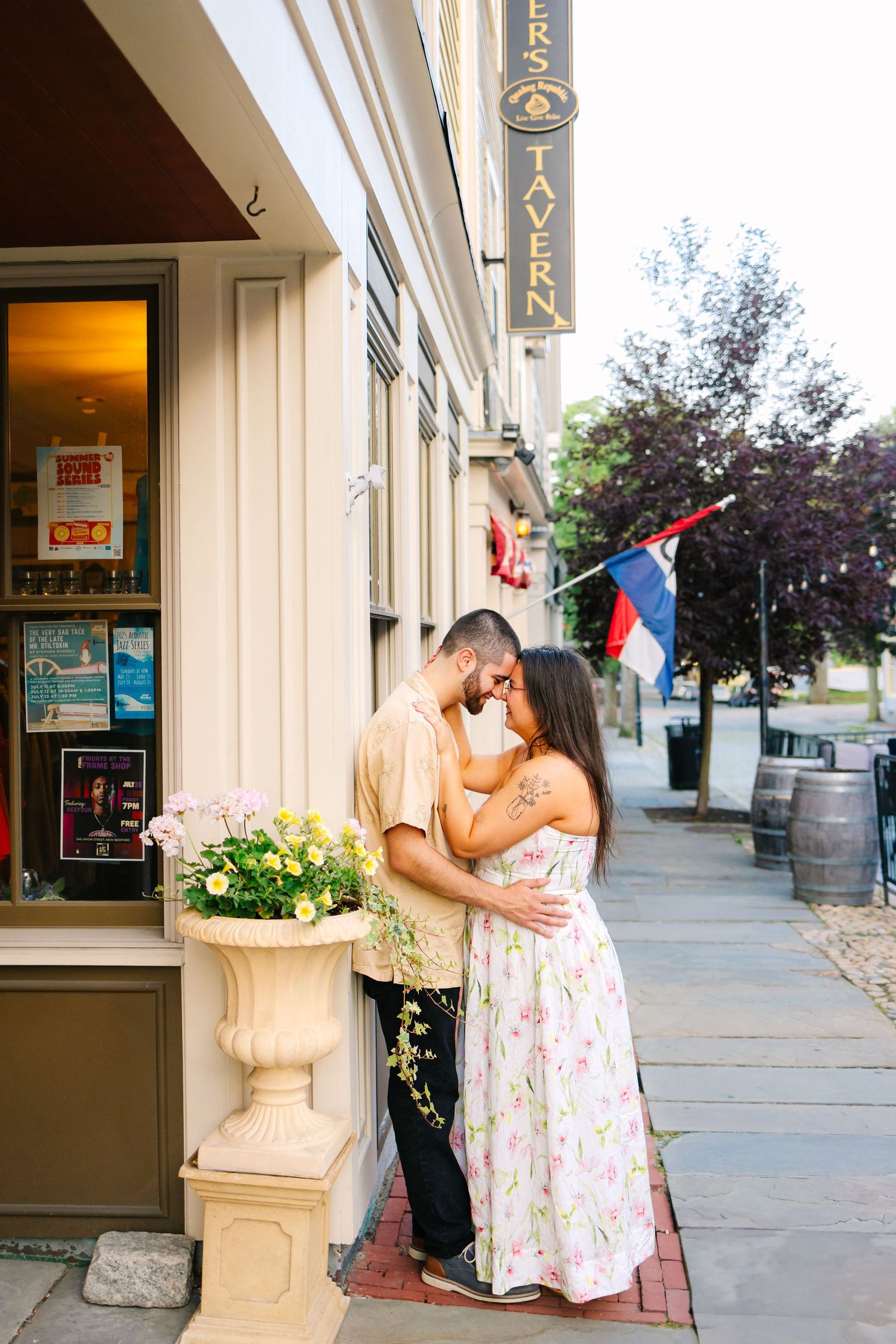 Couple shares romantic kisses outside a storefront with stone columns in Downtown New Bedford Massachusetts for engagement photos
