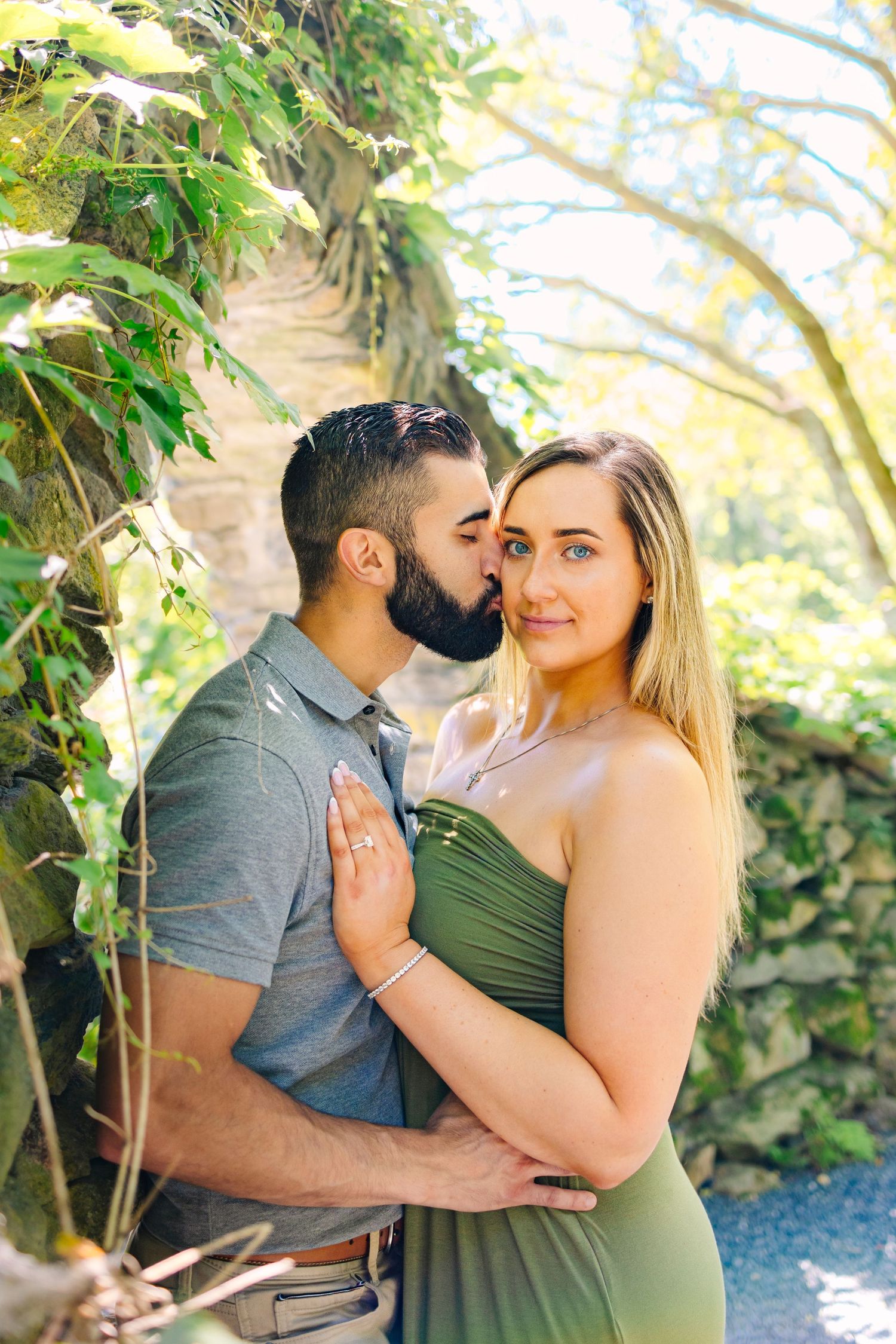 A couple embraces in a romantic garden setting with lush greenery and natural sunlight surrounding them at Blithewold Mansion in Bristol RI