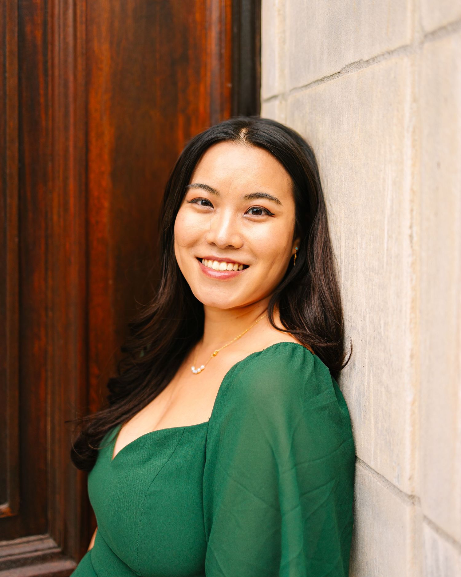 College grad wearing an emerald green top poses with a warm smile against a school building at Brown University in Providence Rhode Island