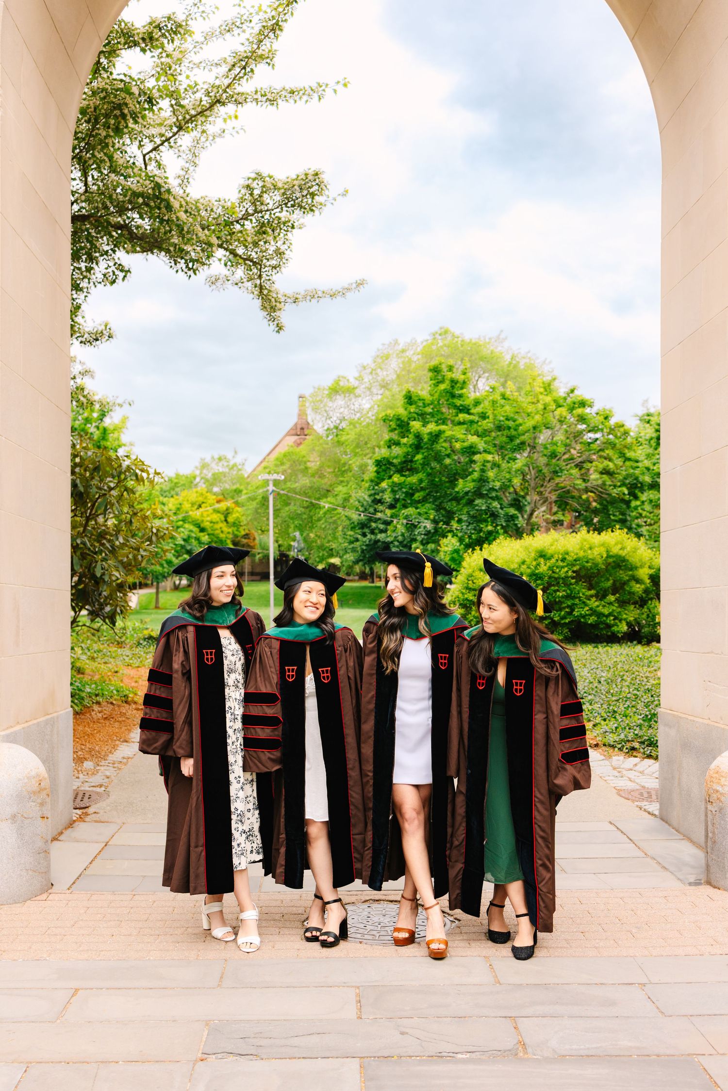 Graduates in traditional brown academic robes and caps walking through a covered outdoor colonnade at Brown University Rhode Island