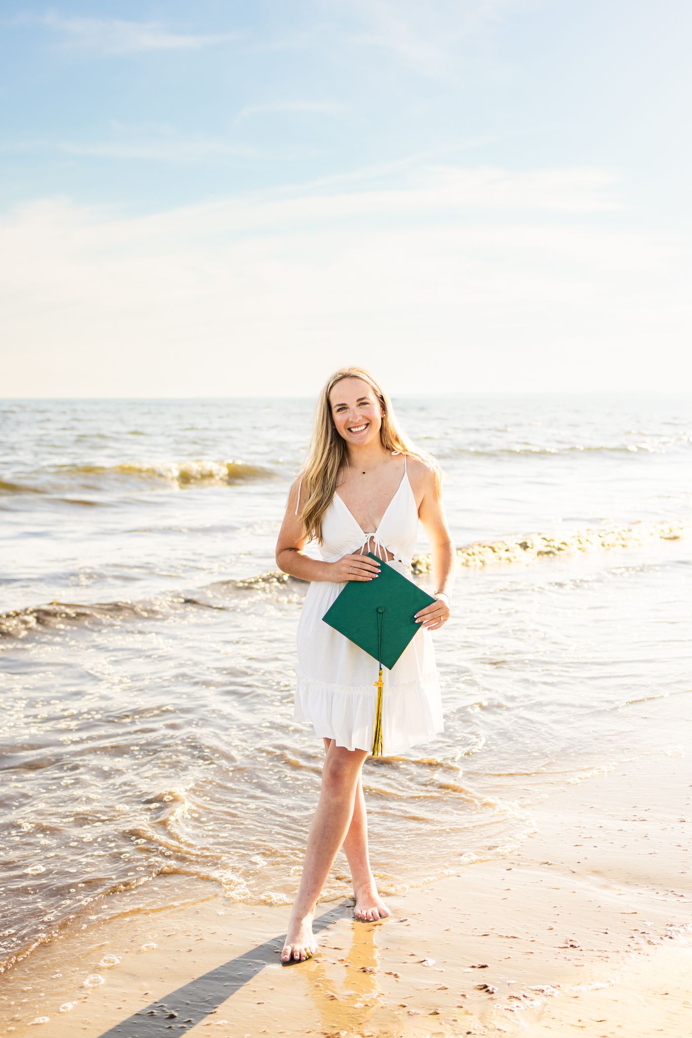 High school senior holding graduation cap by the shoreline during sunset golden hour at Horseneck Beach in Westport Massachusetts