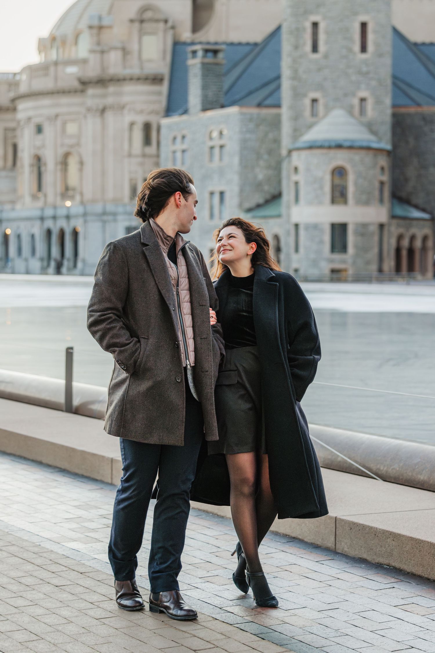 A couple in winter coats sharing a joyful moment while walking along a stone path at the Back Bay in Boston, Massachusetts
