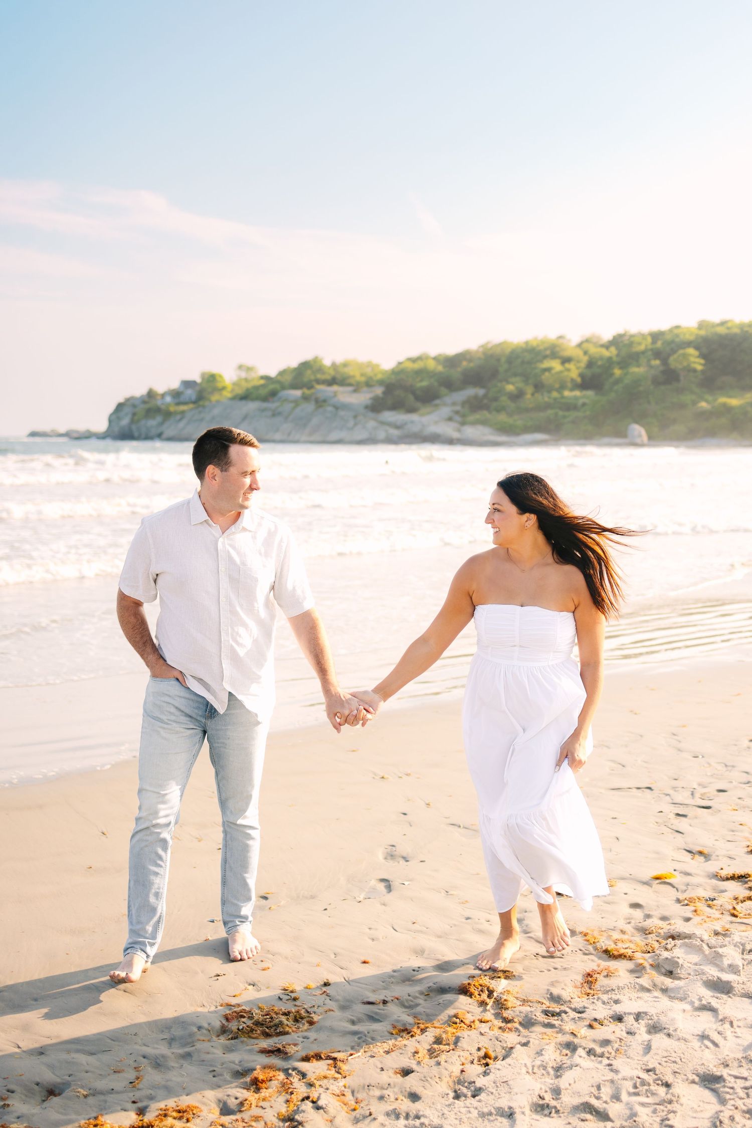 A couple walking along the shore during sunset golden hour for engagement photos at Second Beach in Newport, Rhode Island