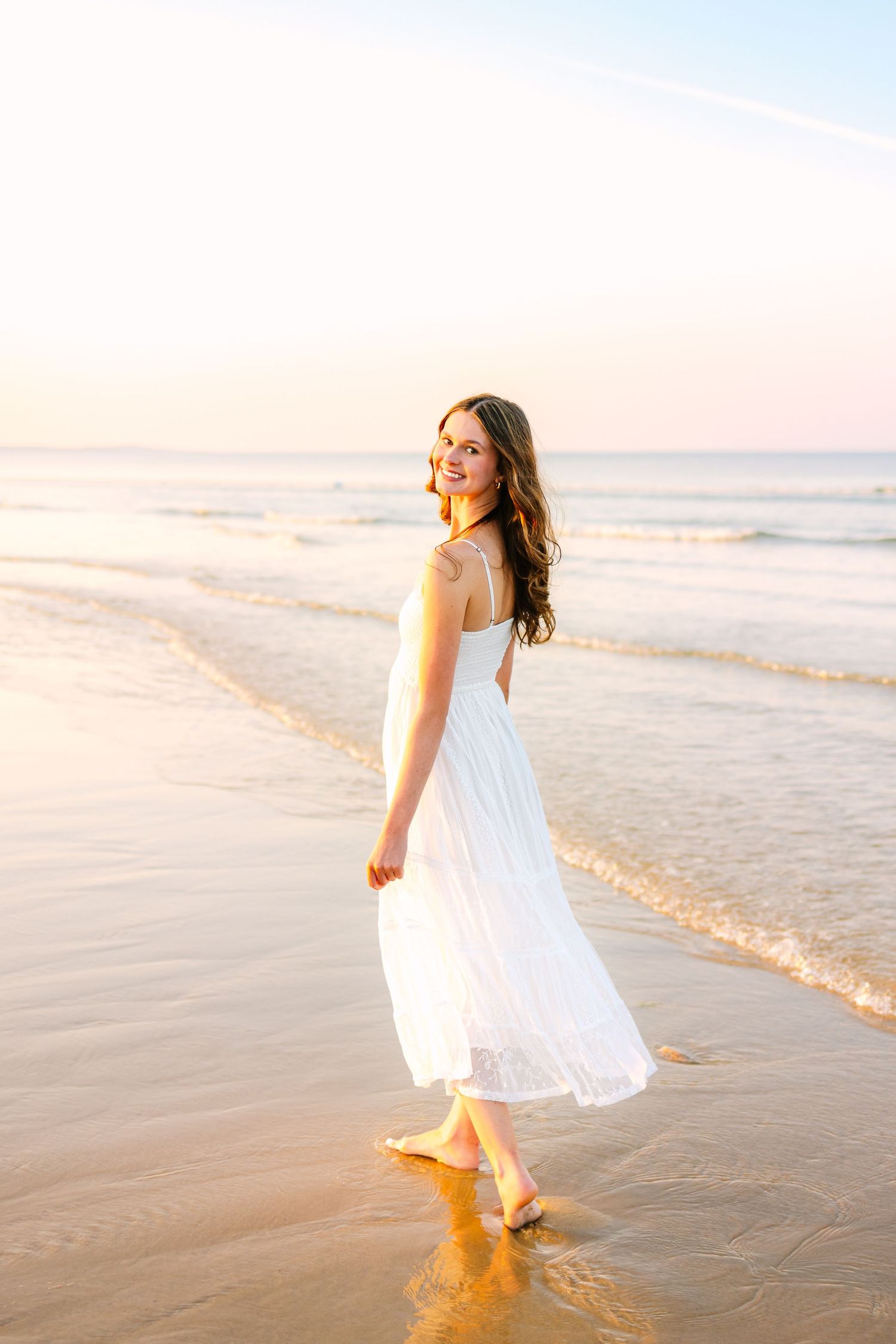A high school senior twirls joyfully along beach shoreline at sunset creating dreamy senior photos at Scusset Beach in Cape Cod Mass