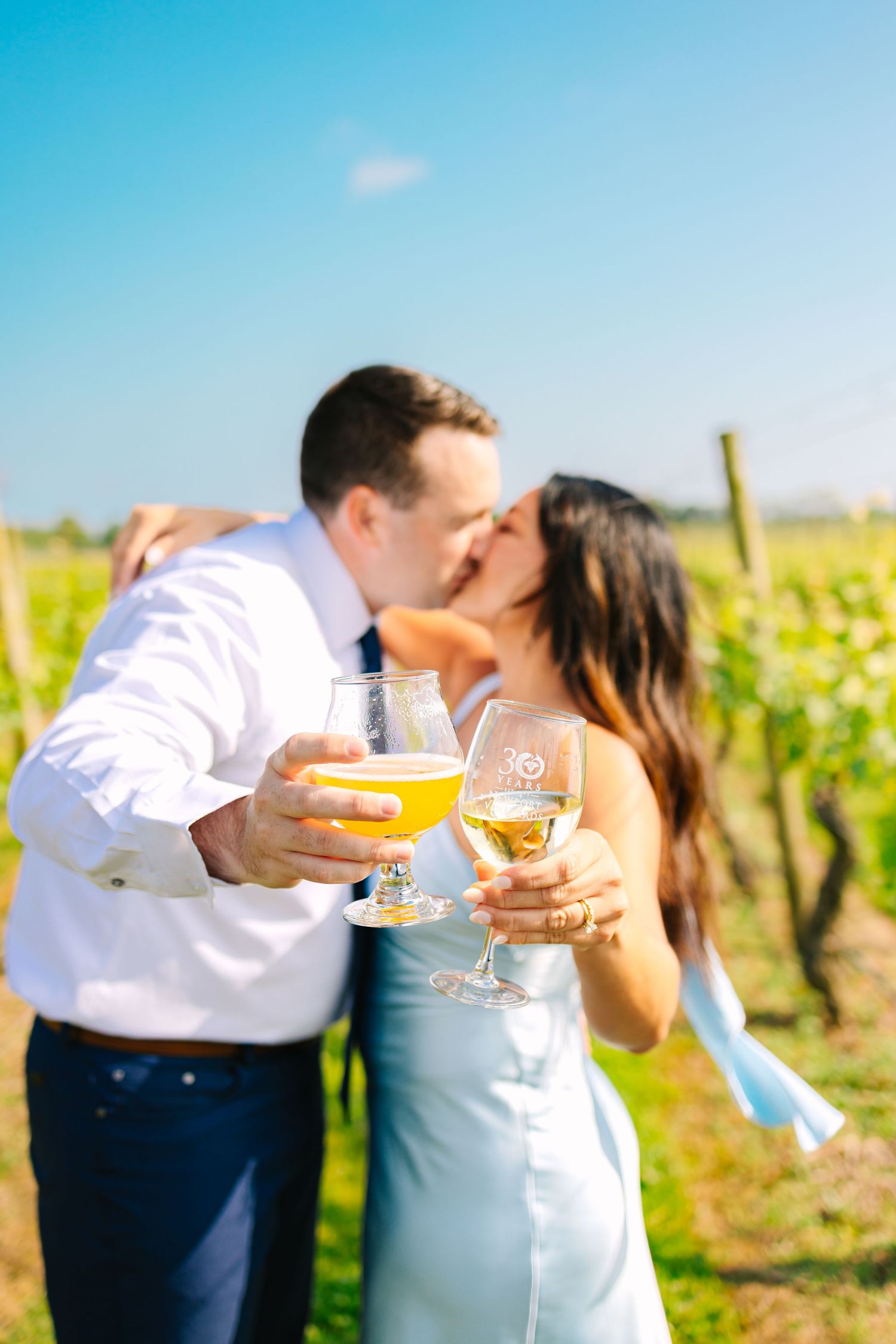 Romantic couple toasting and kissing at a sunny vineyard with wine glasses in hand on a bright summer day at Newport Vineyards in RI
