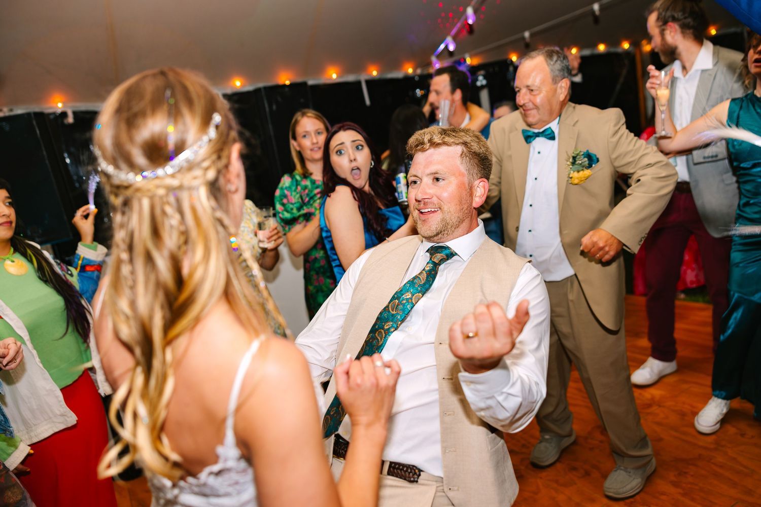 Wedding guests dance and celebrate together on a lively dance floor during an evening reception celebration.