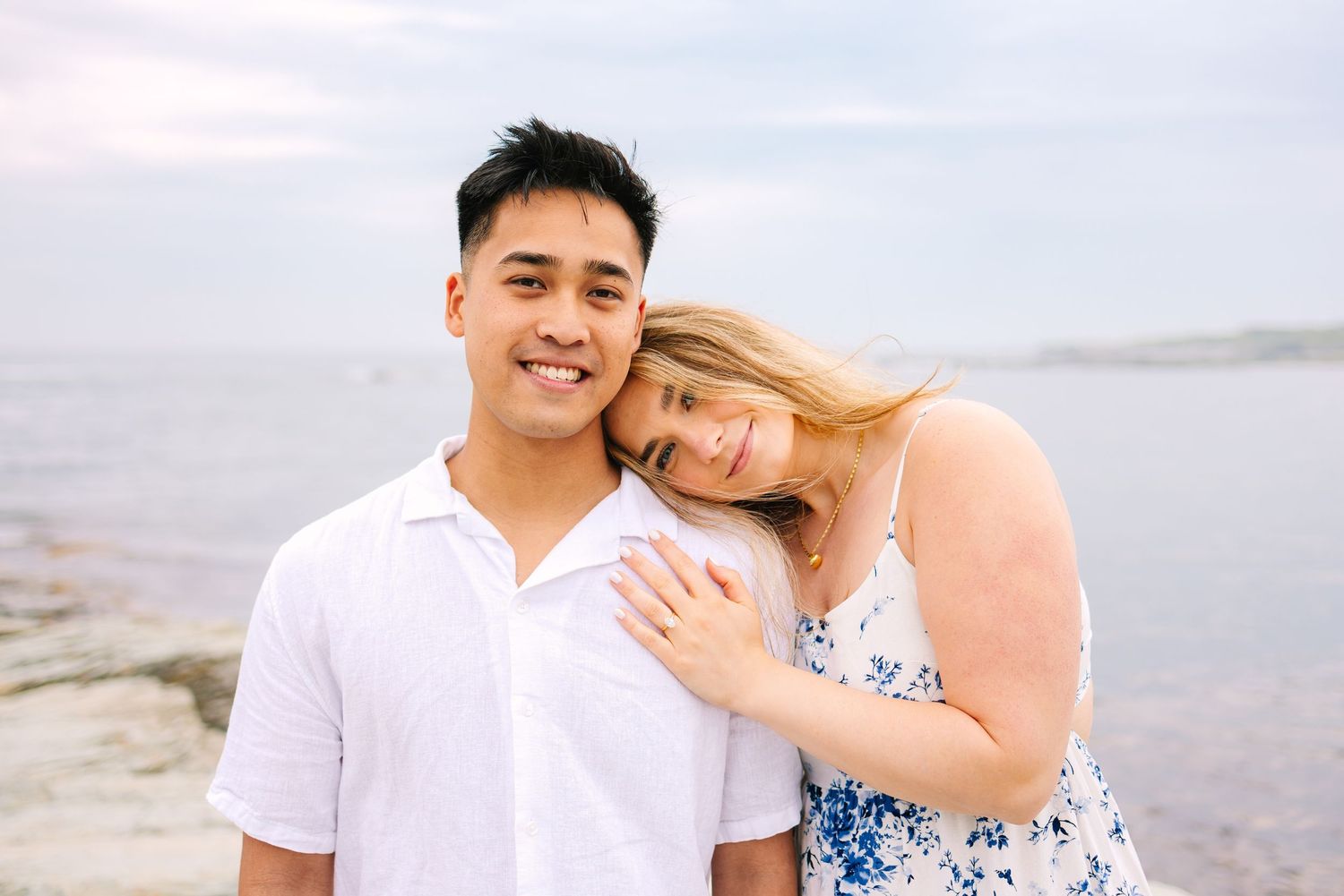 A couple poses affectionately together on a rocky coastal cliff for engagement photos at sunset on Ocean Drive in Newport Rhode Island