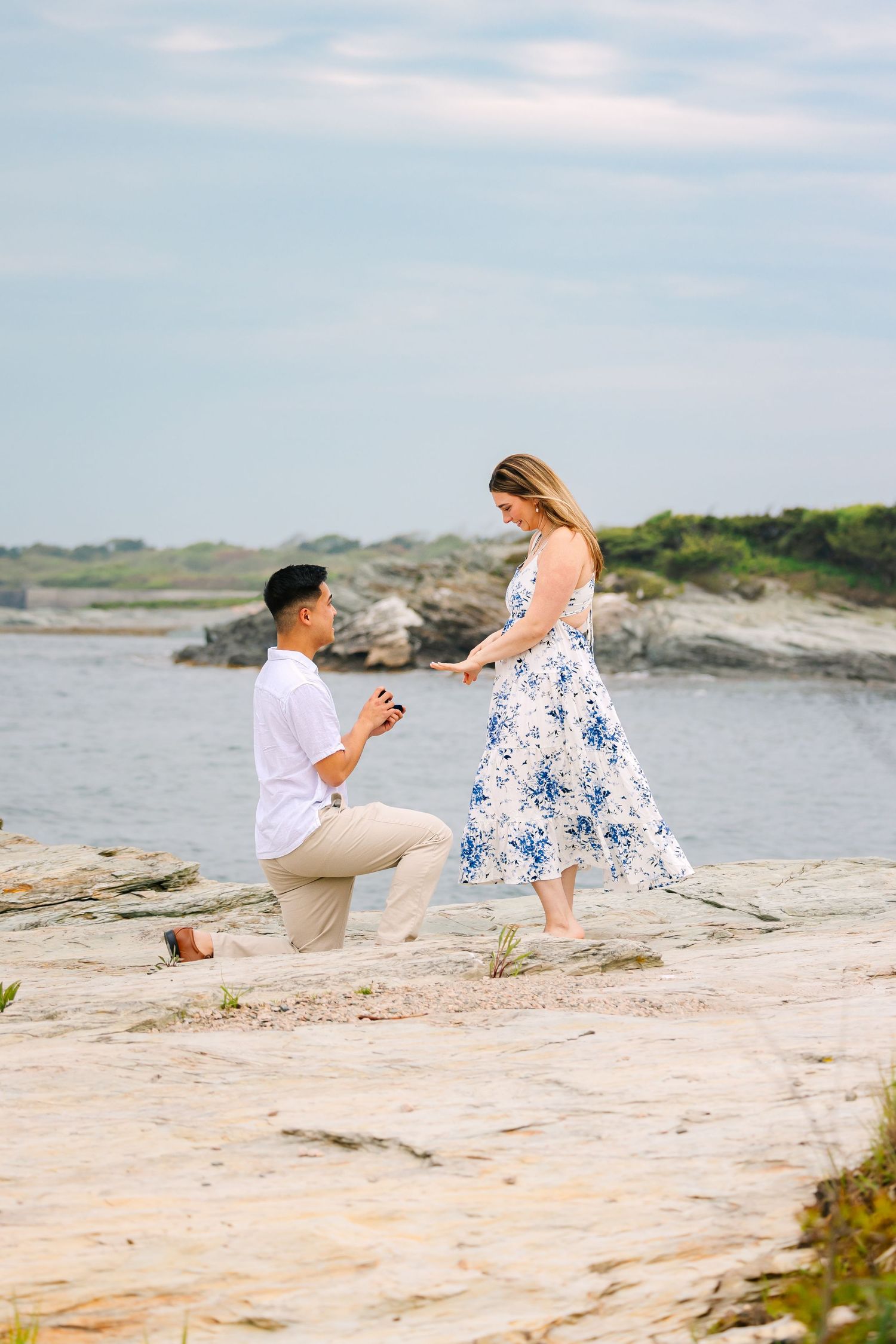 A romantic proposal scene on a rocky coastal cliff area at sunset on Ocean Drive in Newport Rhode Island