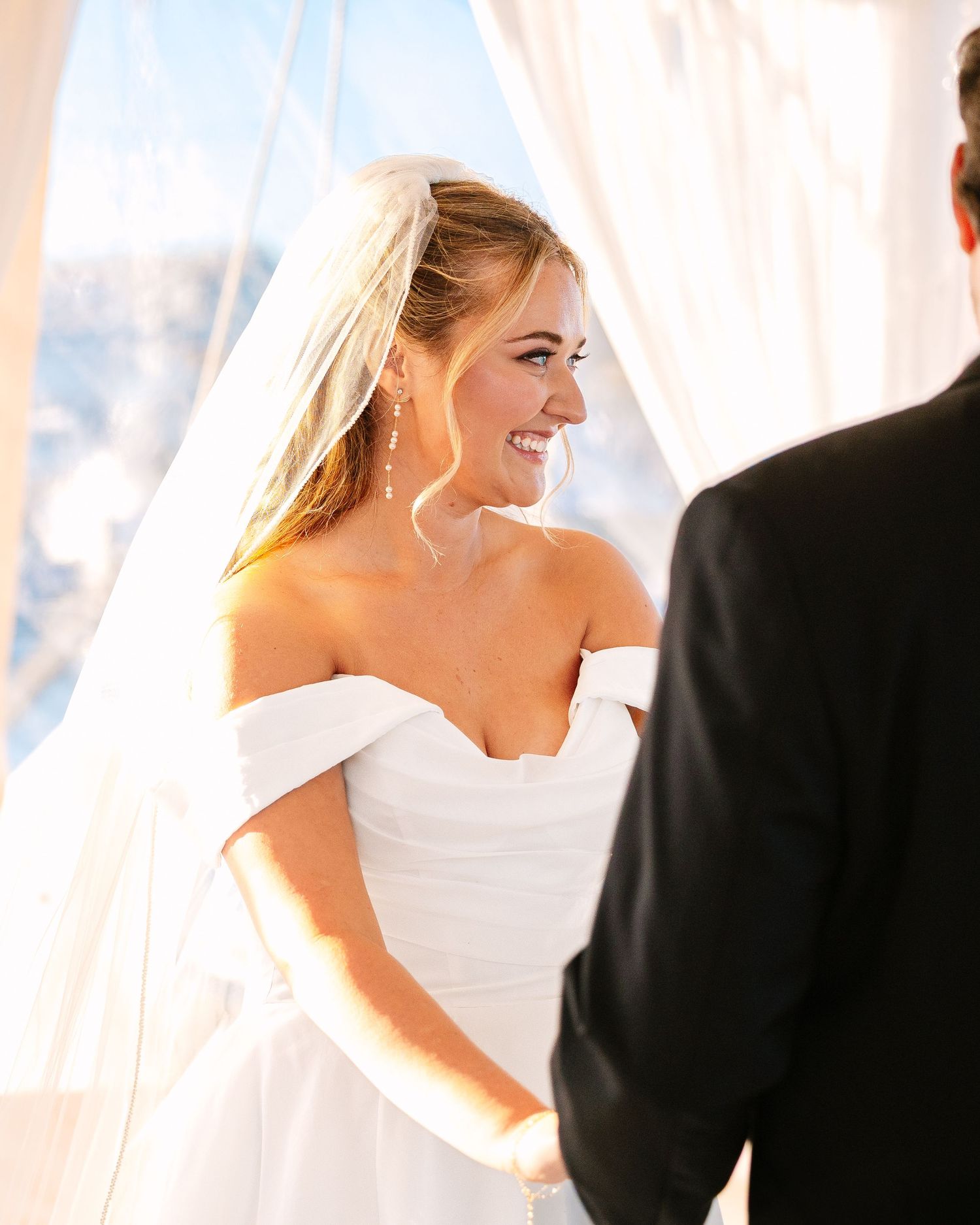 Bride and groom share a joyful moment together under white drapes during their wedding ceremony.