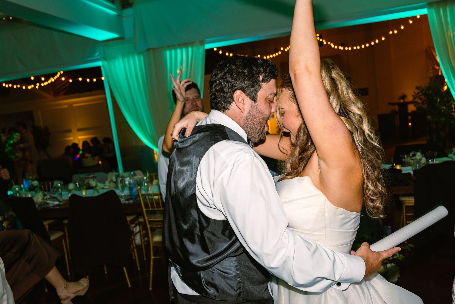 A bride and groom dancing together at a wedding reception with green ambient lighting and decorative string lights at The Regatta Place RI