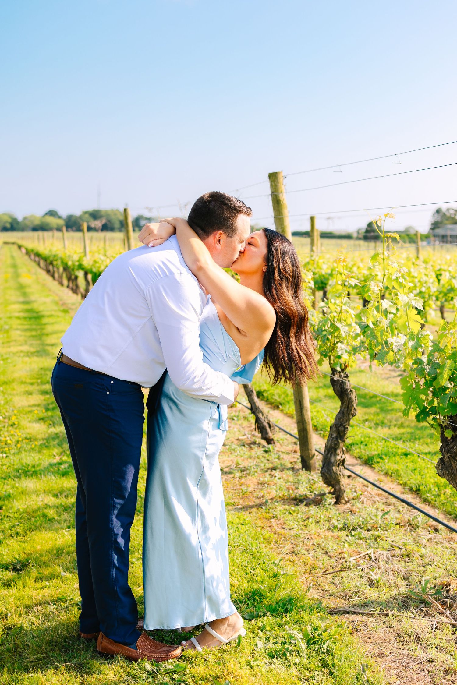 Romantic couple embraces in a sun-drenched vineyard with rows of grape vines stretching into the distance at Newport Vineyards in Newport RI