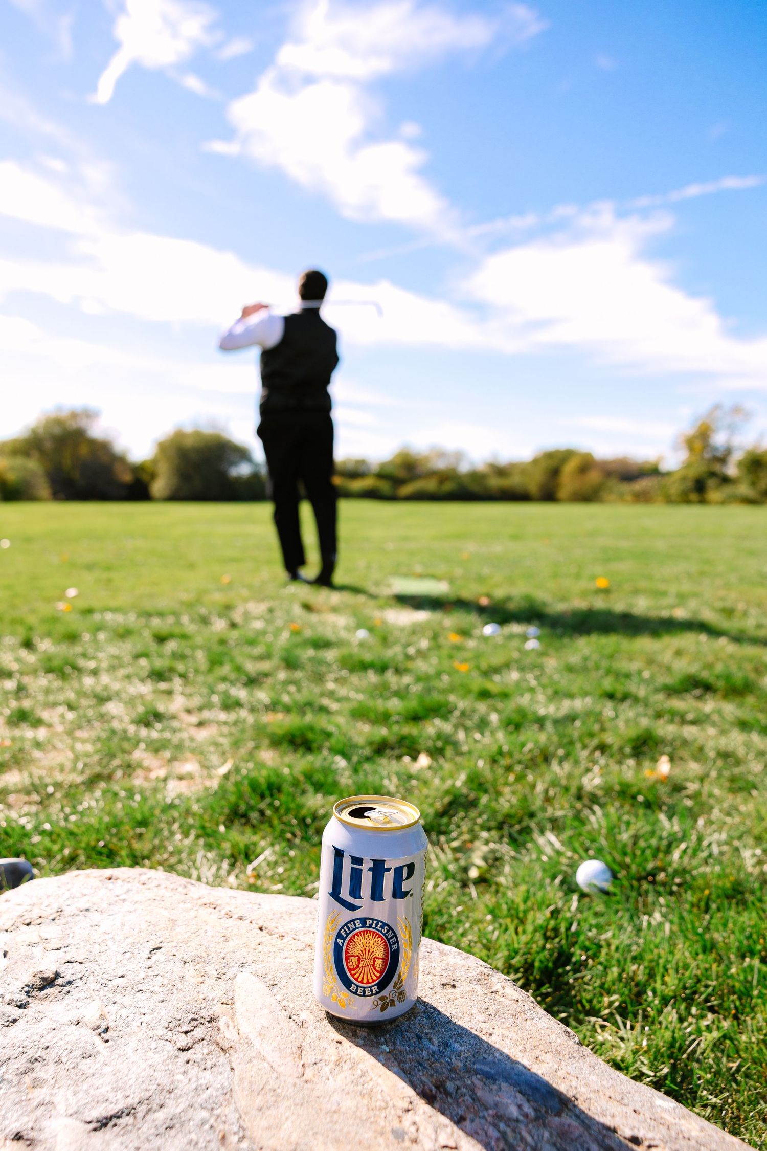Beer cans sit in sand traps on a sunny golf course with a silhouetted figure in the background.