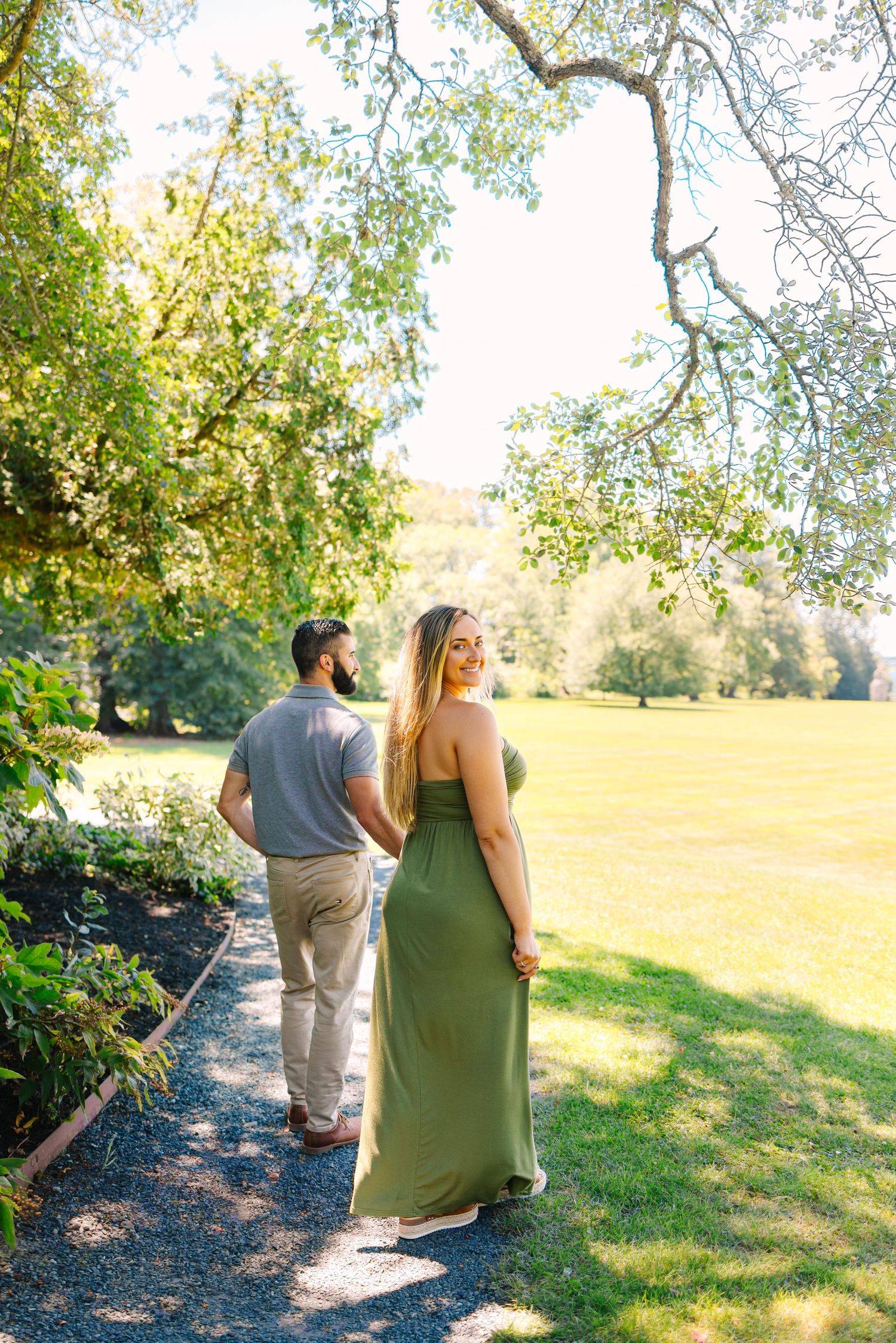 Couple walking along a garden path on a sunny day with green grass and overhanging trees in the background at Blithewold Mansion in RI