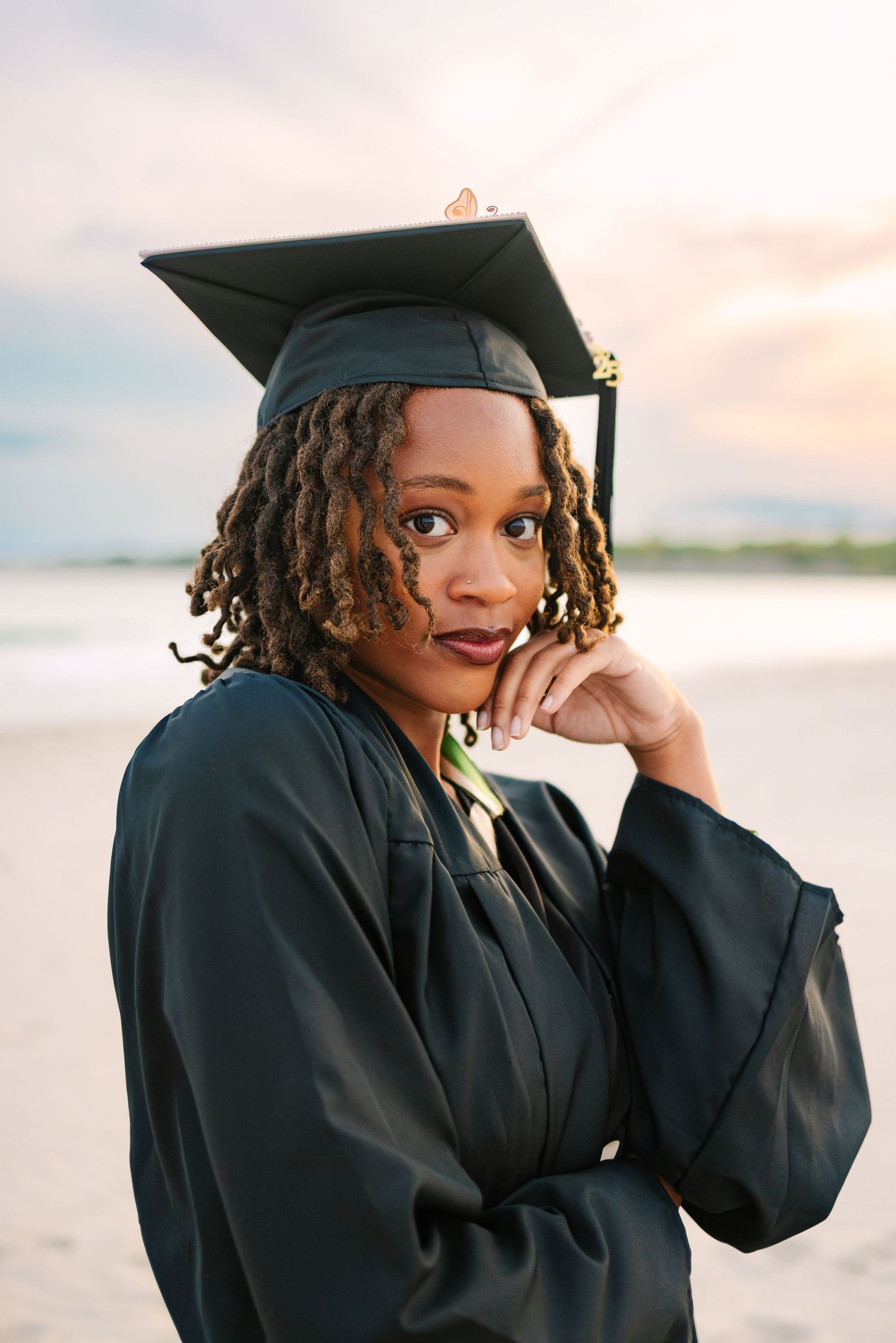 A graduate in cap and gown poses on the beach at sunset golden hour for grad photos at Second Beach Newport Rhode Island Salve Regina