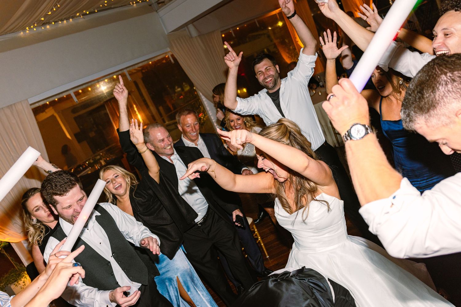 Wedding guests dance and celebrate on a crowded dance floor at a reception party with decorative lighting at The Regatta Place in Newport RI