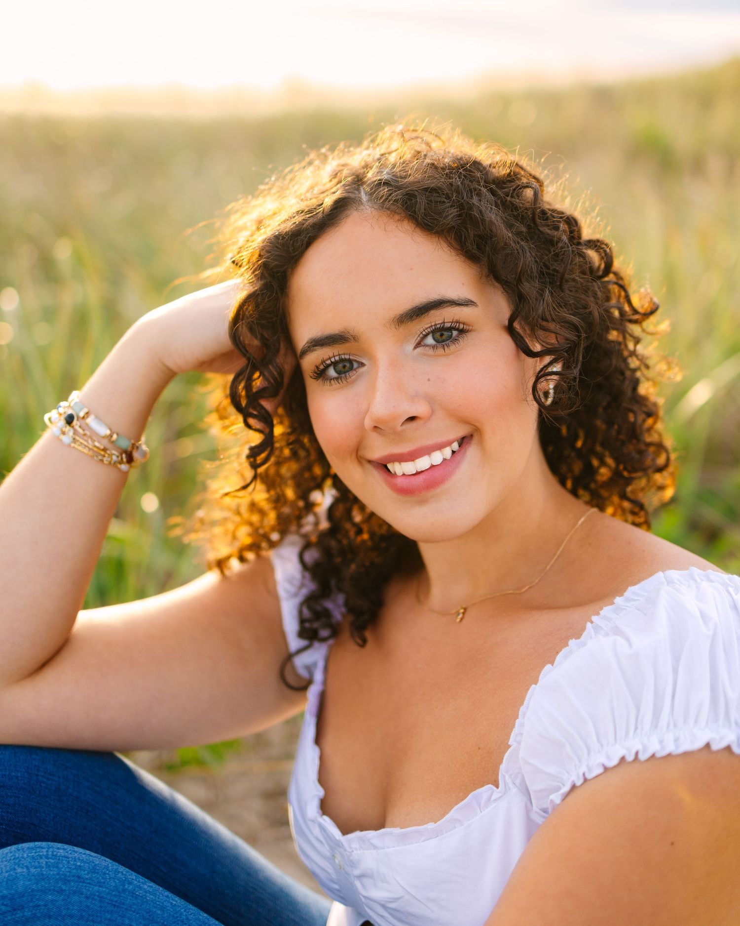 A high school senior at golden hour with curly hair against natural coastal vegetation for senior photos at Horseneck Beach in Westport MA
