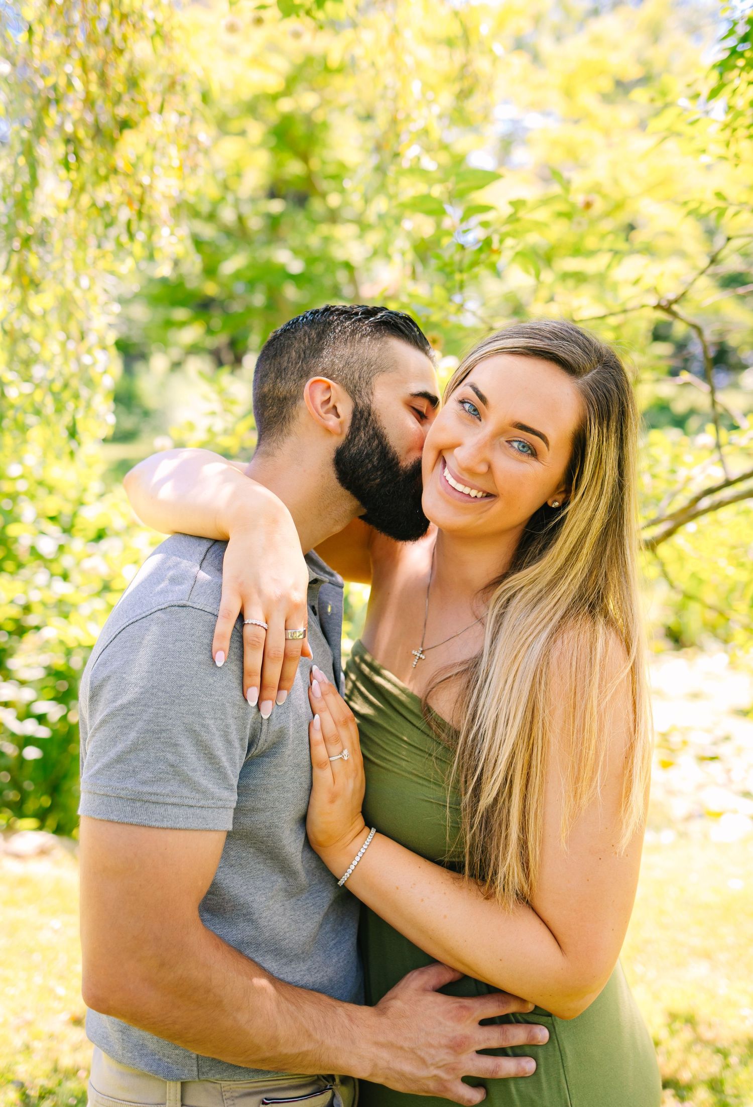 Romantic couple embraces outdoors on a sunny summer day after a surprise proposal at Blithewold Mansion in Bristol Rhode Island