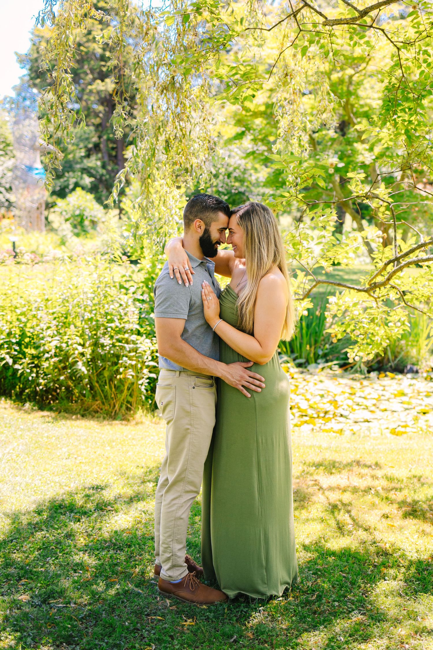 A romantic couple embraces under a weeping willow tree on a sunny day in a lush garden setting at Blithewold Mansion in Bristol Rhode Island