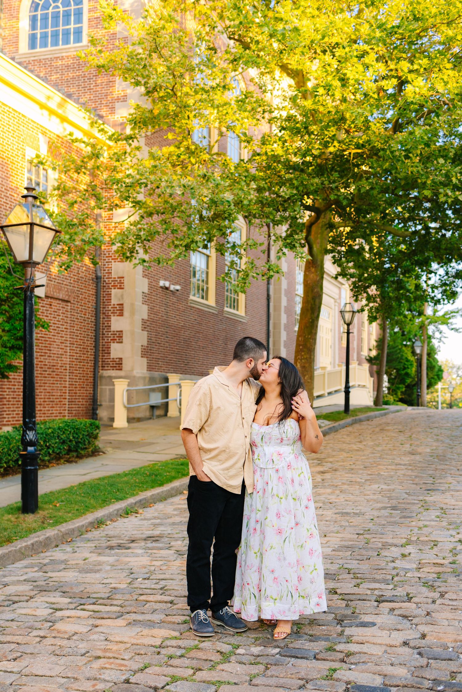 A couple shares an intimate moment on a cobblestone path beside a historic brick building for engagement photos in New Bedford Massachusetts