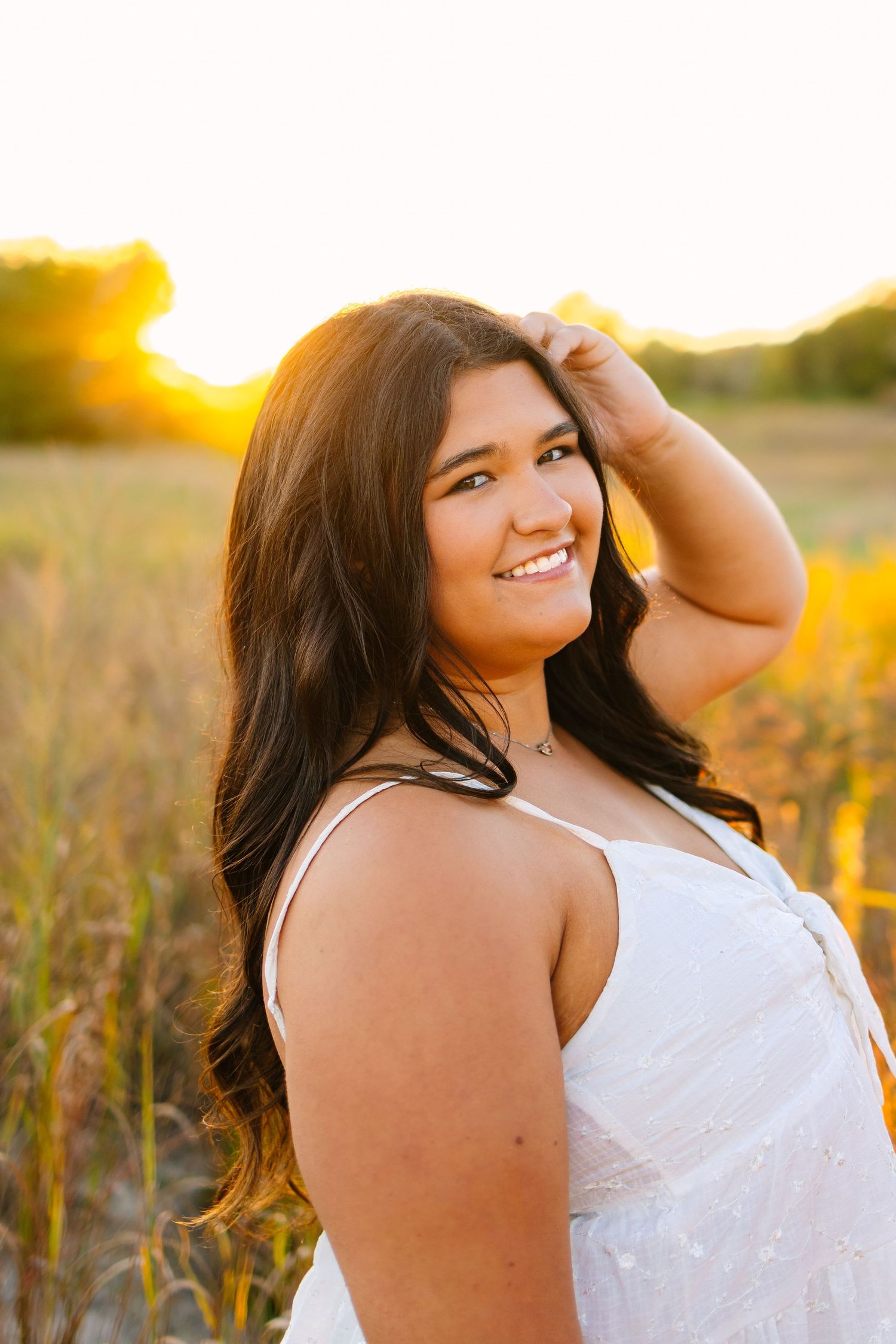A high school senior poses in a golden field during sunset with warm lighting and natural scenery for senior photos in West Greenwich RI
