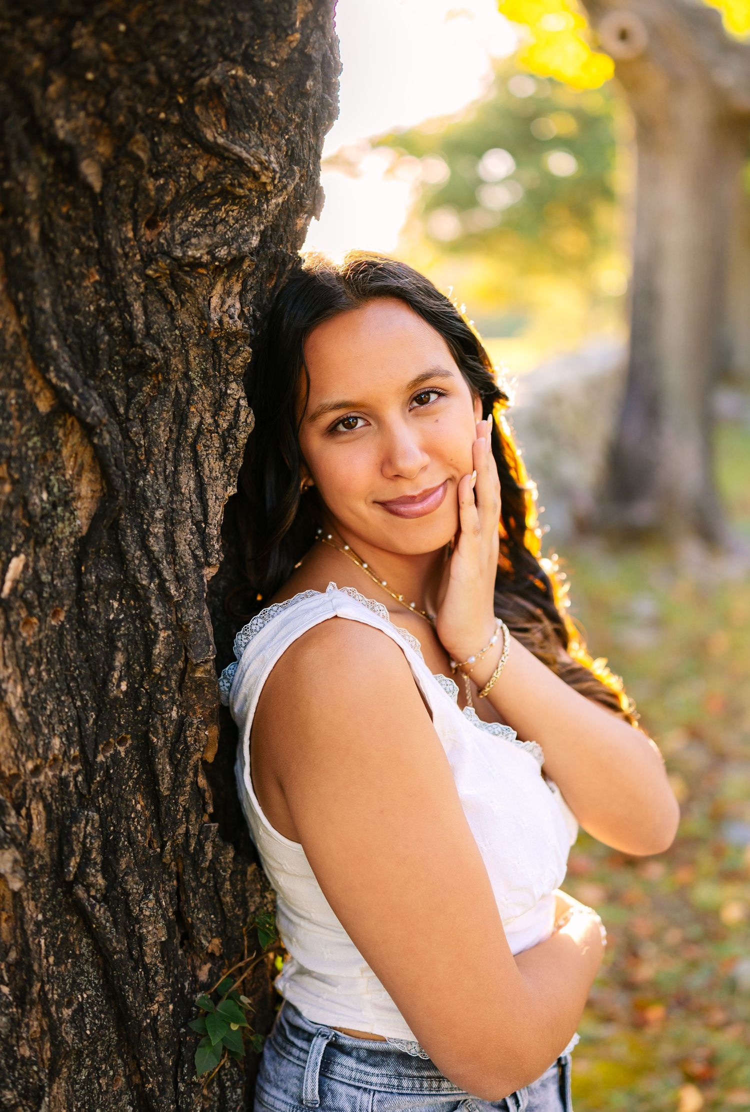 A high school senior in a park during golden hour with autumn leaves and tree trunks for senior photos at Colt State Park in Bristol RI