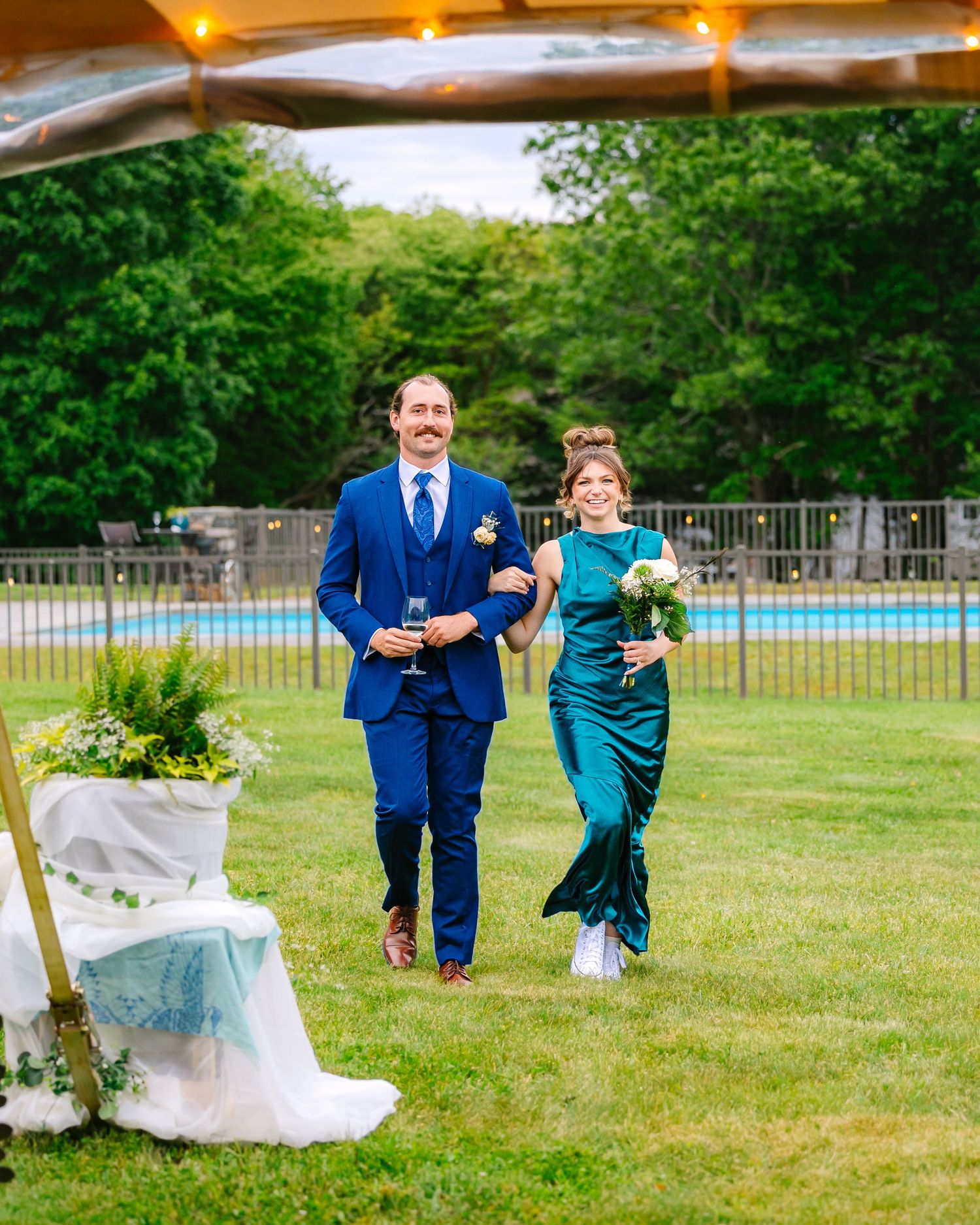 Wedding party members walk together across a green lawn during an outdoor summer celebration.