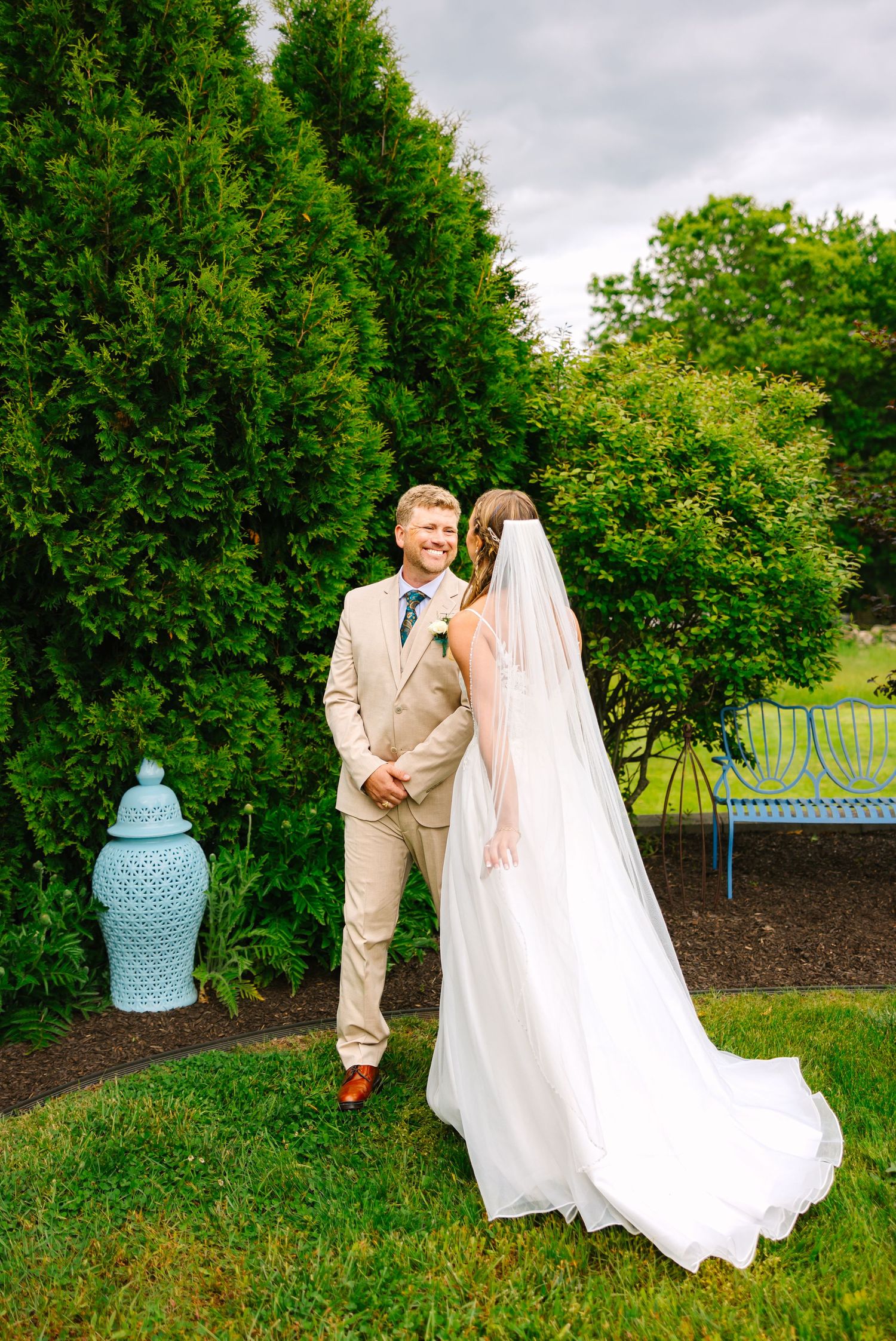 A couple shares a joyful moment in a garden setting with lush greenery and a decorative blue vase in the background.