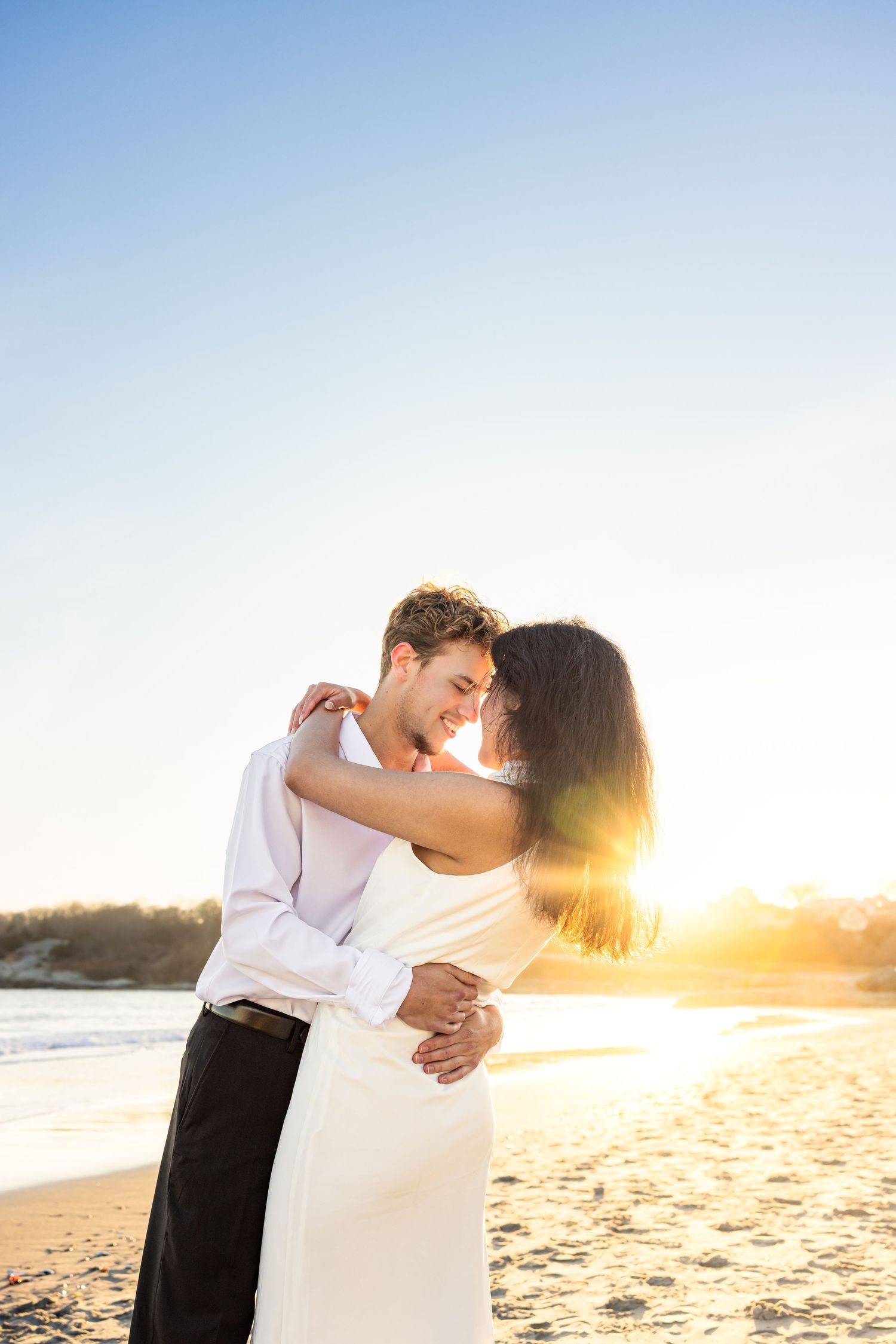 A romantic couple embraces on a beach at sunset with golden sunlight streaming through their silhouettes at Second Beach in Newport RI