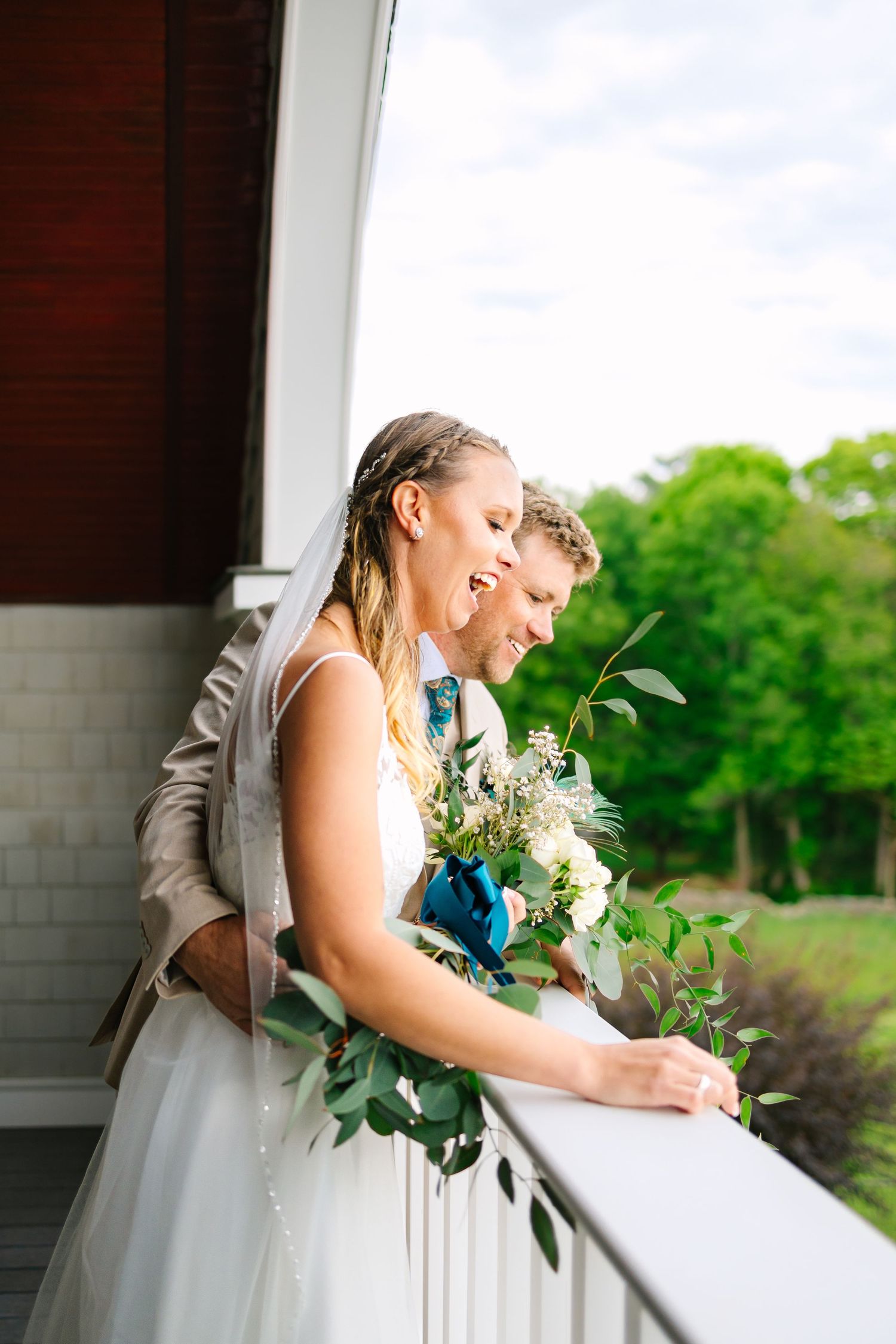 Wedding couple in formal attire sharing a romantic moment on a porch with white bouquet and greenery at backyard wedding reception in CT