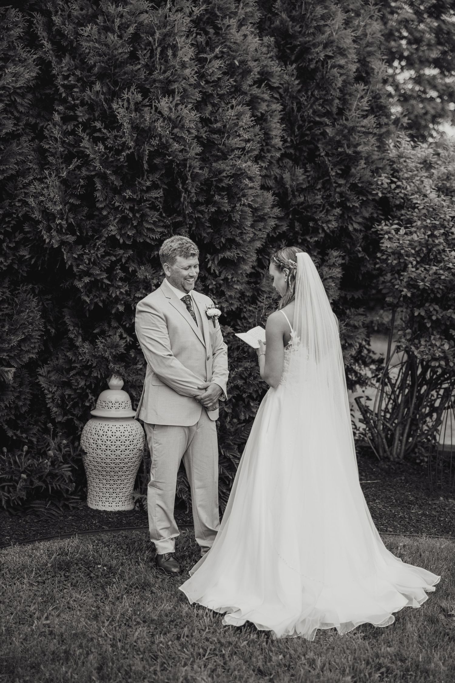 A couple shares a tender moment on their wedding day in a garden setting with lush greenery in the background.