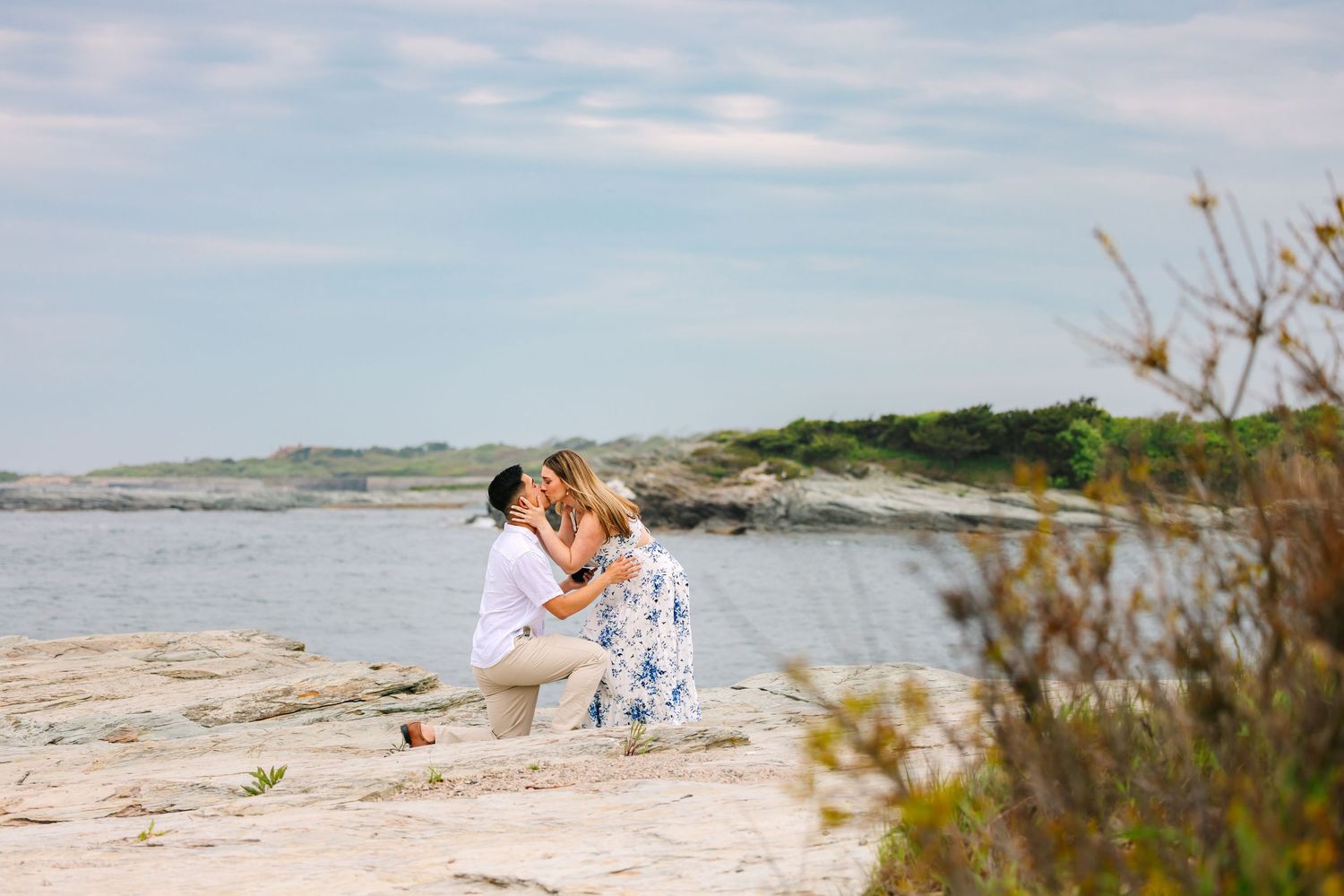 Couple sharing a romantic kiss on rocky New England shoreline during a beach engagement photo session in Newport Rhode Island