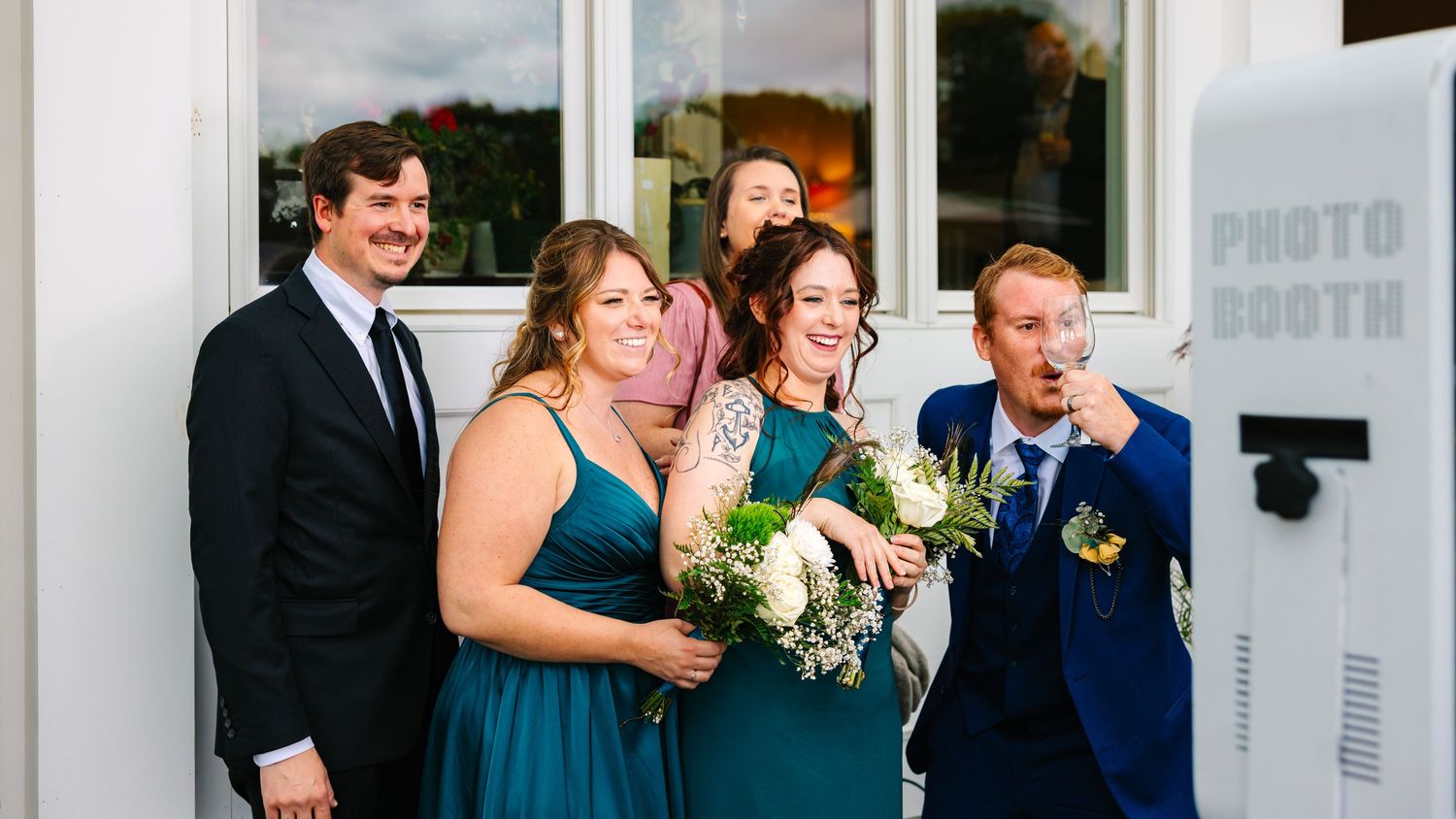 A group of people in formal attire pose together in front of a white photo booth at an event.