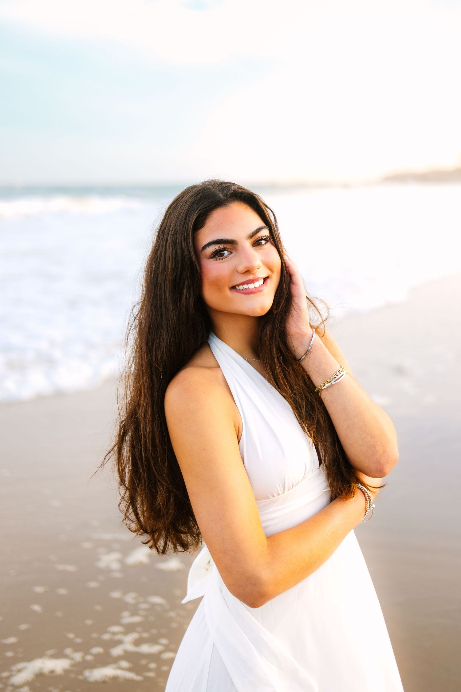 A high school senior stands along the shoreline at sunset golden hour for senior photos at Manchester By The Sea in Boston Massachusetts