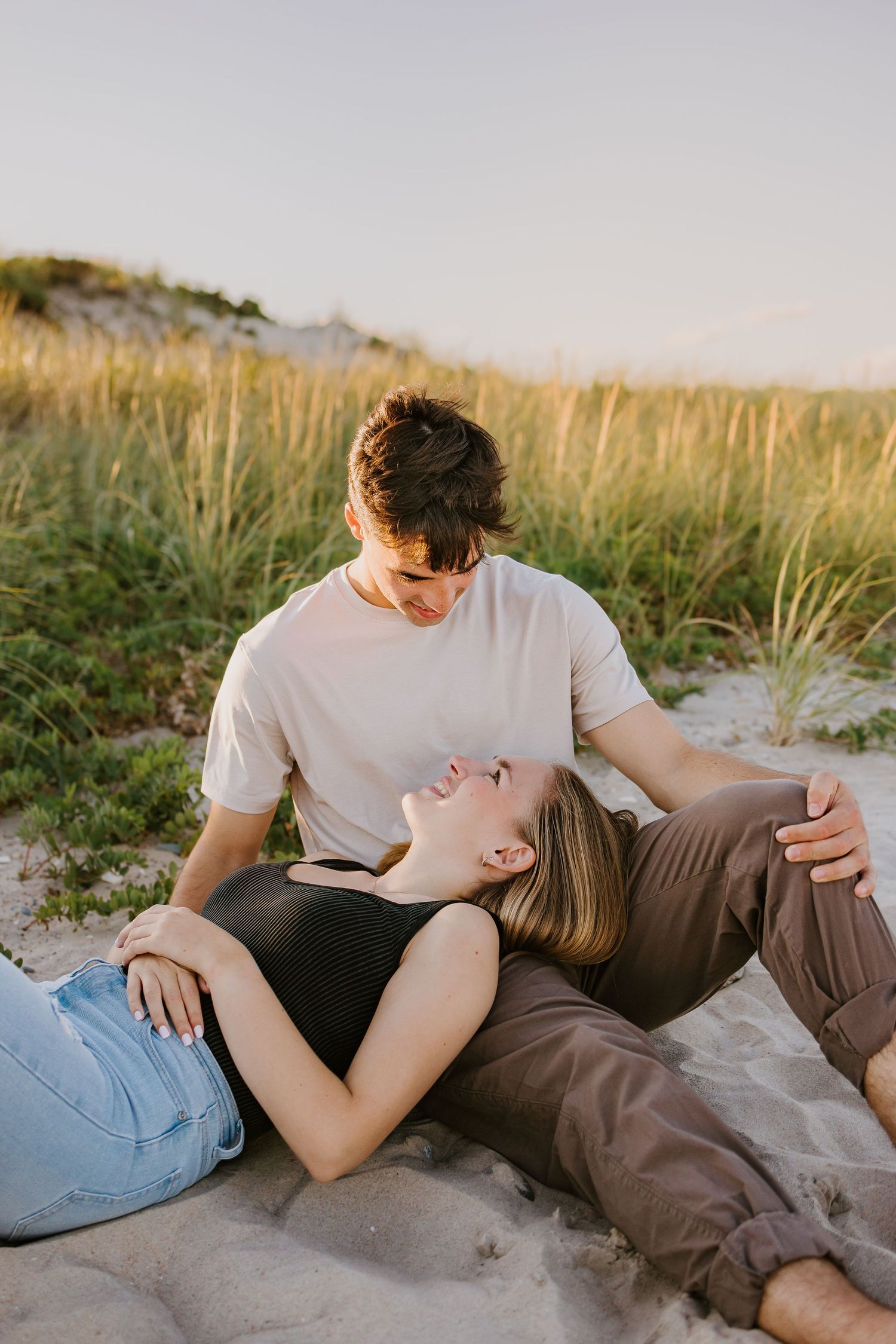 A couple shares an intimate moment while relaxing together on sandy beach dunes at sunset golden hour at Horseneck Beach in Westport MA