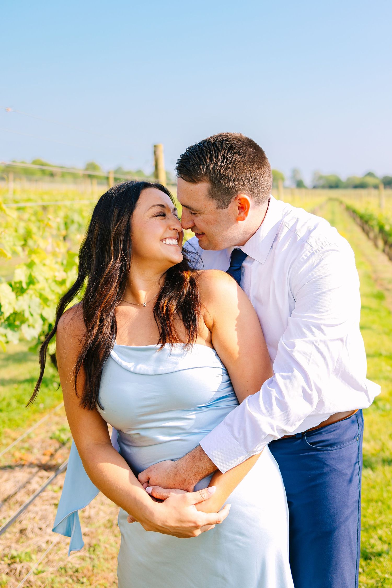 A couple embraces in a sunny vineyard during a romantic summer engagement photoshoot at Newport Vineyards in Newport Rhode Island