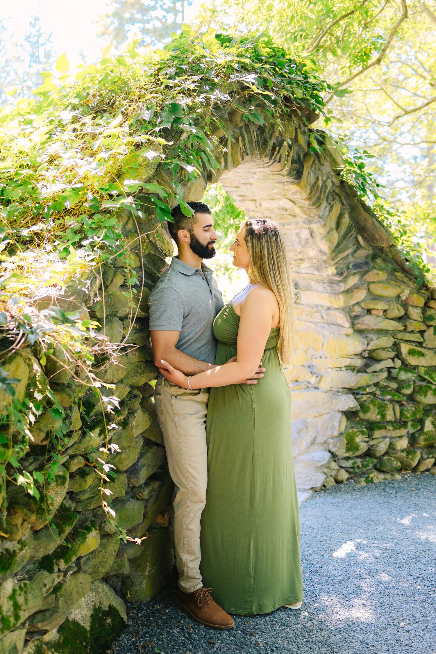 A couple embraces beneath a ivy-covered stone archway in a romantic garden setting.