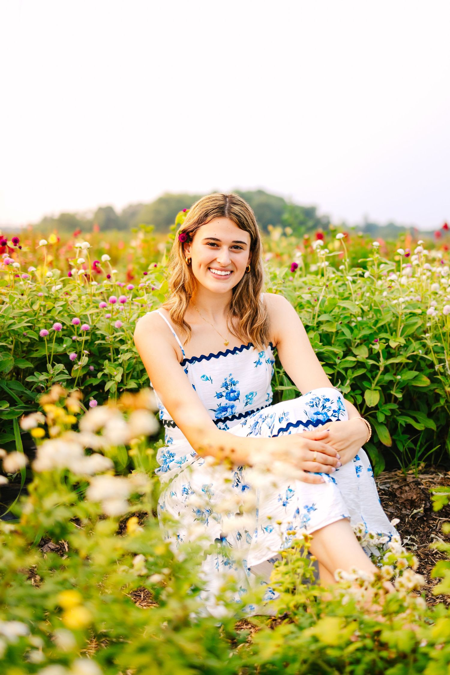 A high school senior sits by colorful wildflowers for senior photos during sunset golden hour at Wards Berry Farm in Sharon, Massachusetts