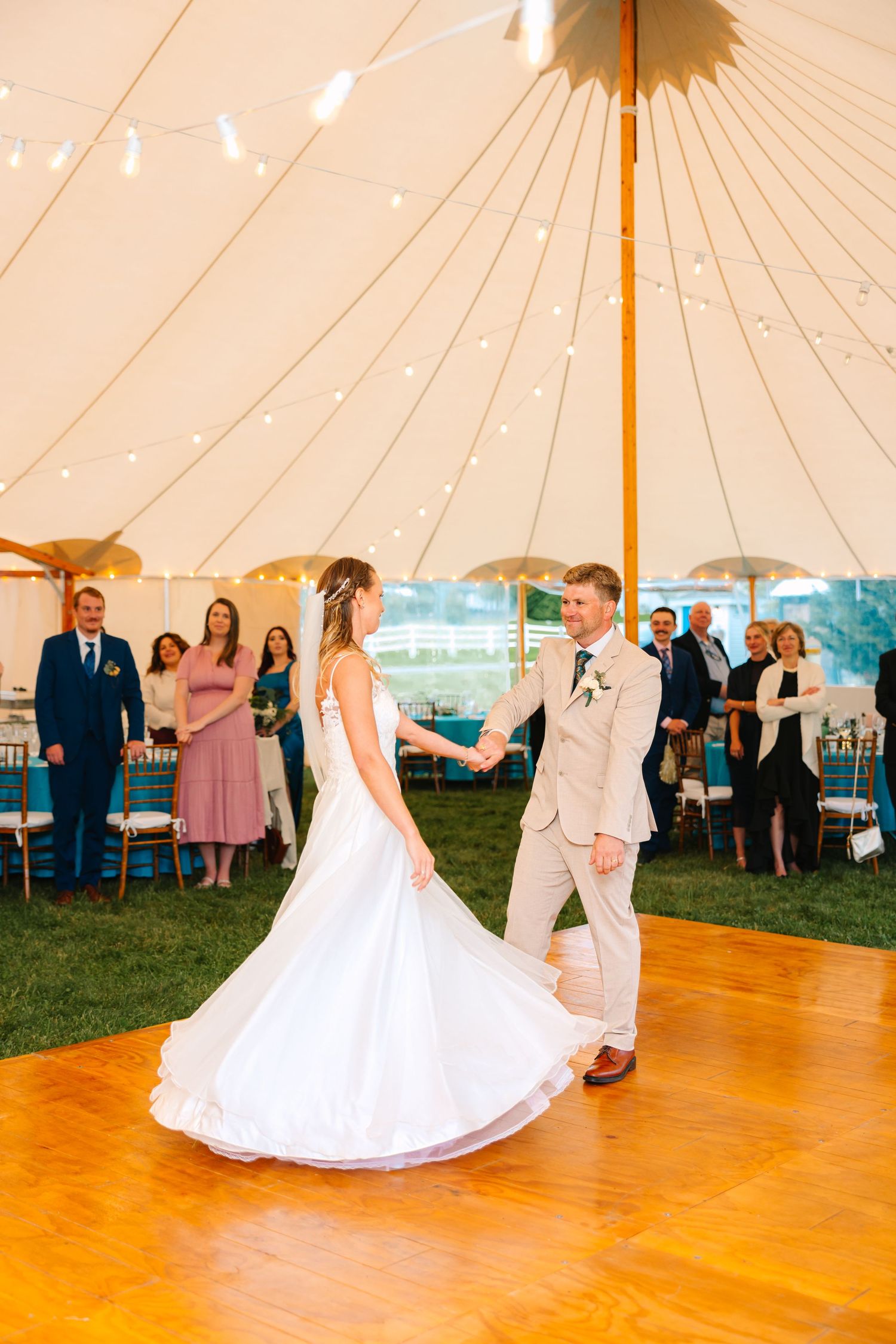 A couple shares their first dance under an elegant white tent during their outdoor wedding reception.