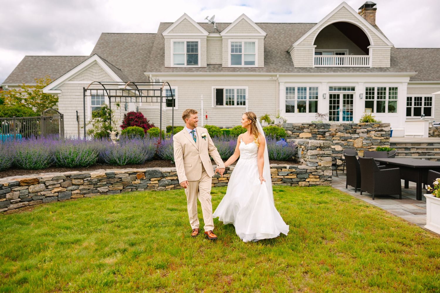 A wedding couple stands on a manicured lawn in front of a luxurious Cape Cod style home for backyard wedding in Stonington Connecticut