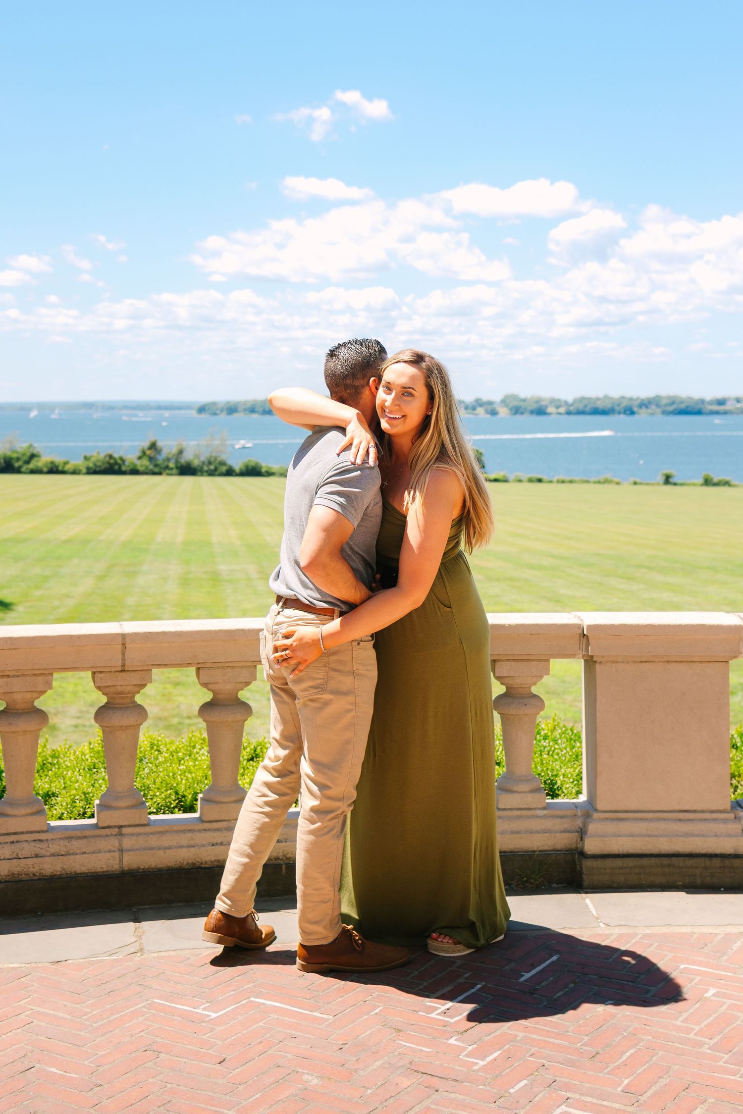 A couple shares a romantic moment on a brick terrace overlooking scenic coastal views on a sunny day.