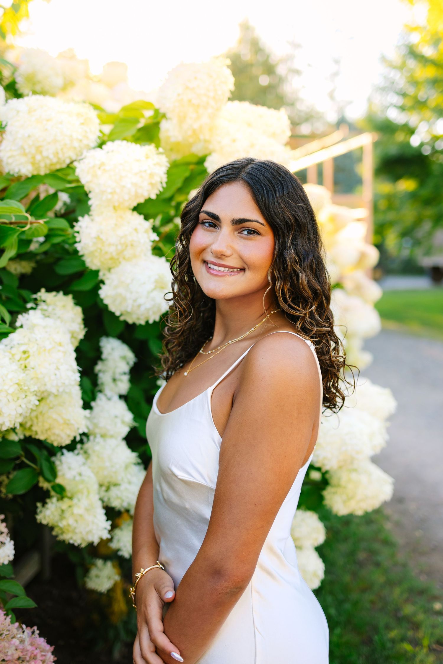 A high school senior posing near a hydrangea bush for senior photos at sunset golden hour at Ward's Berry Farm in Sharon Massachusetts