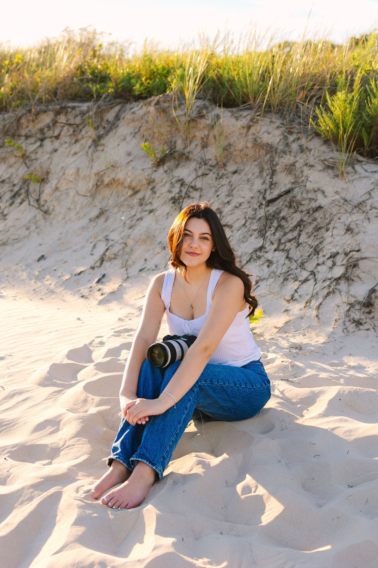 A photographer sitting by the sand dunes holding her camera at sunset golden hour at Horseneck Beach in Westport, Massachusetts