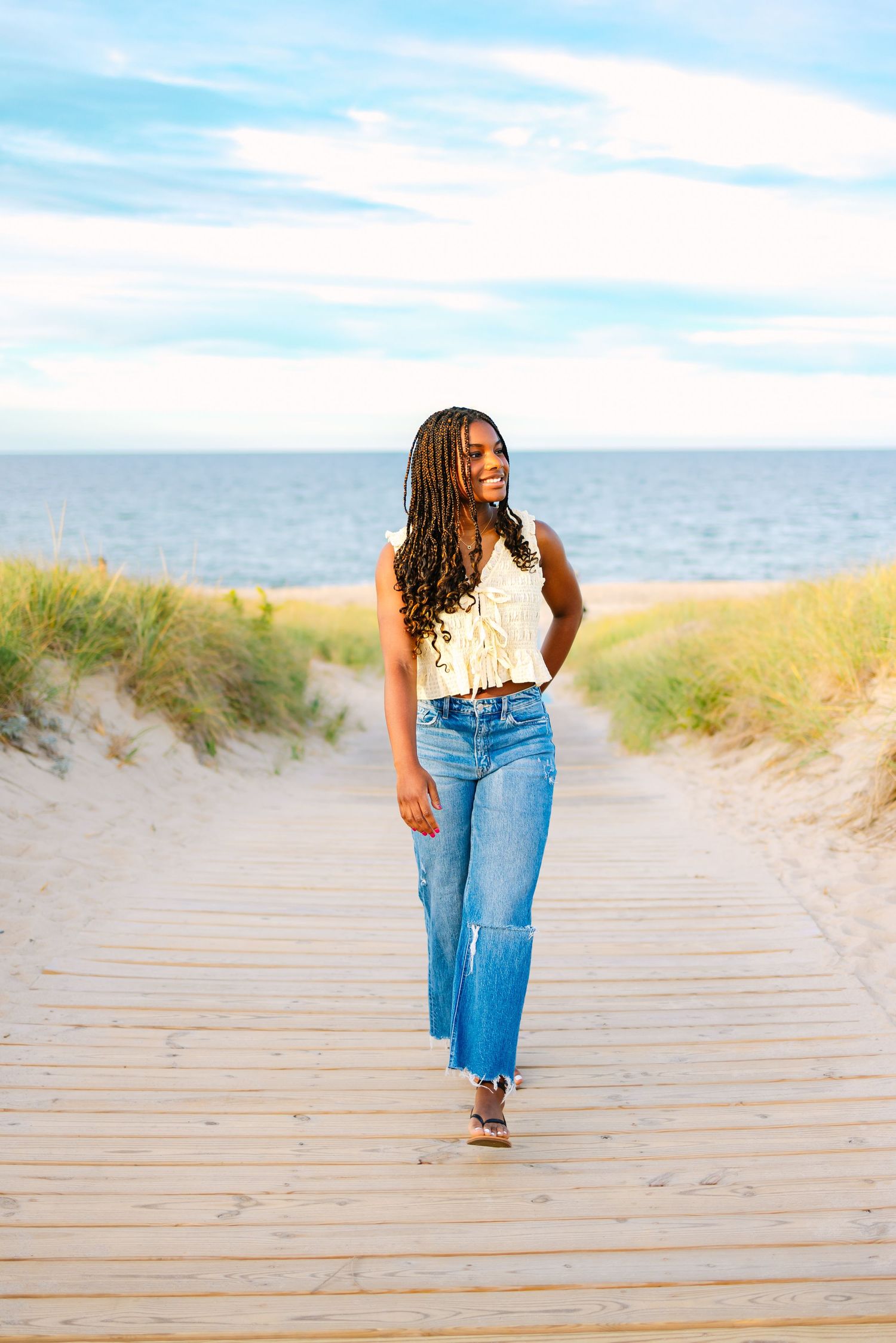 A high school senior walks along a sandy boardwalk during sunset golden hour for senior photos at Scusset Beach in Cape Cod Massachusetts