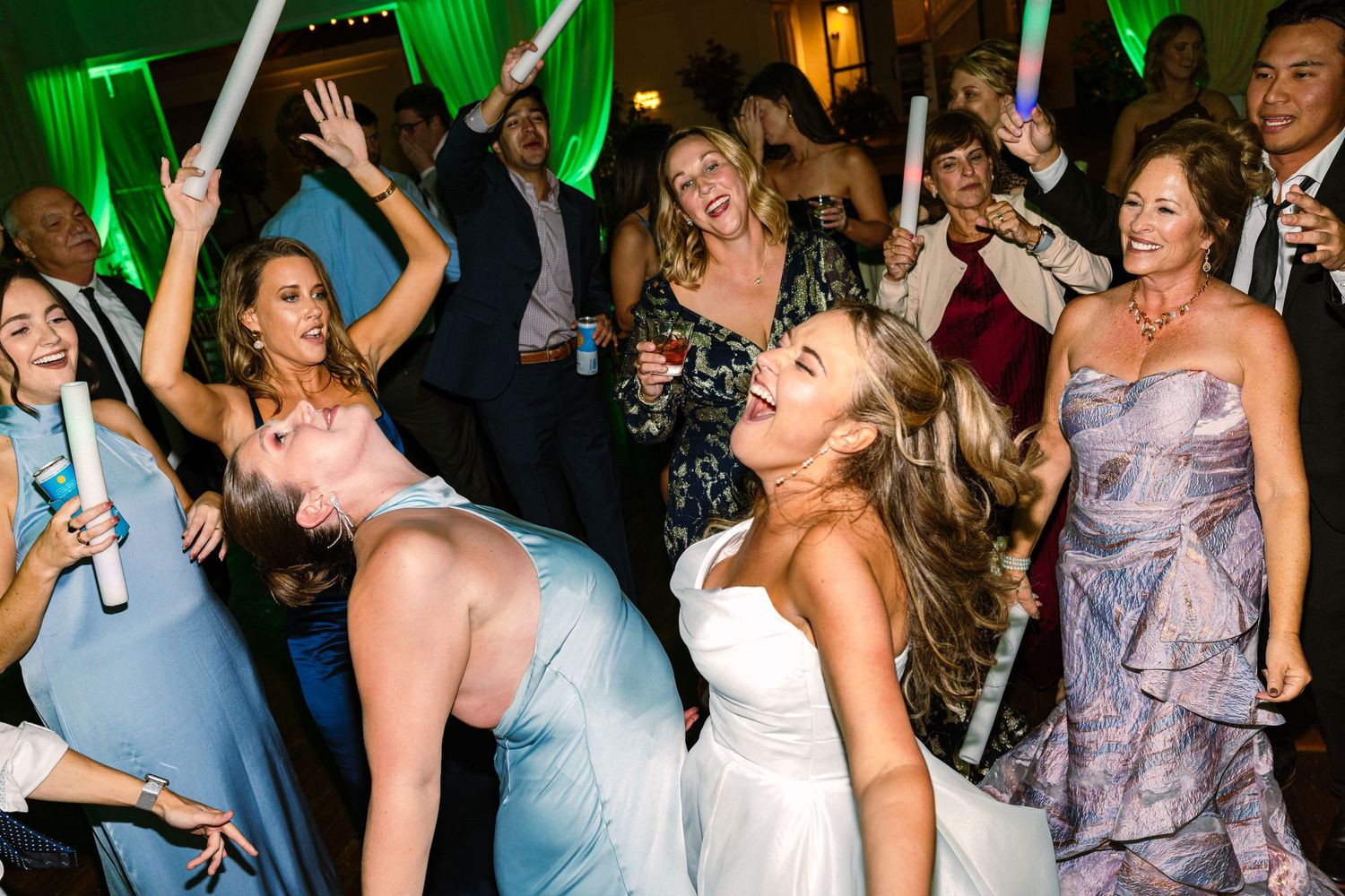 Wedding guests dance and celebrate on a crowded dance floor with green lighting effects in the background at The Regatta Place in Newport RI